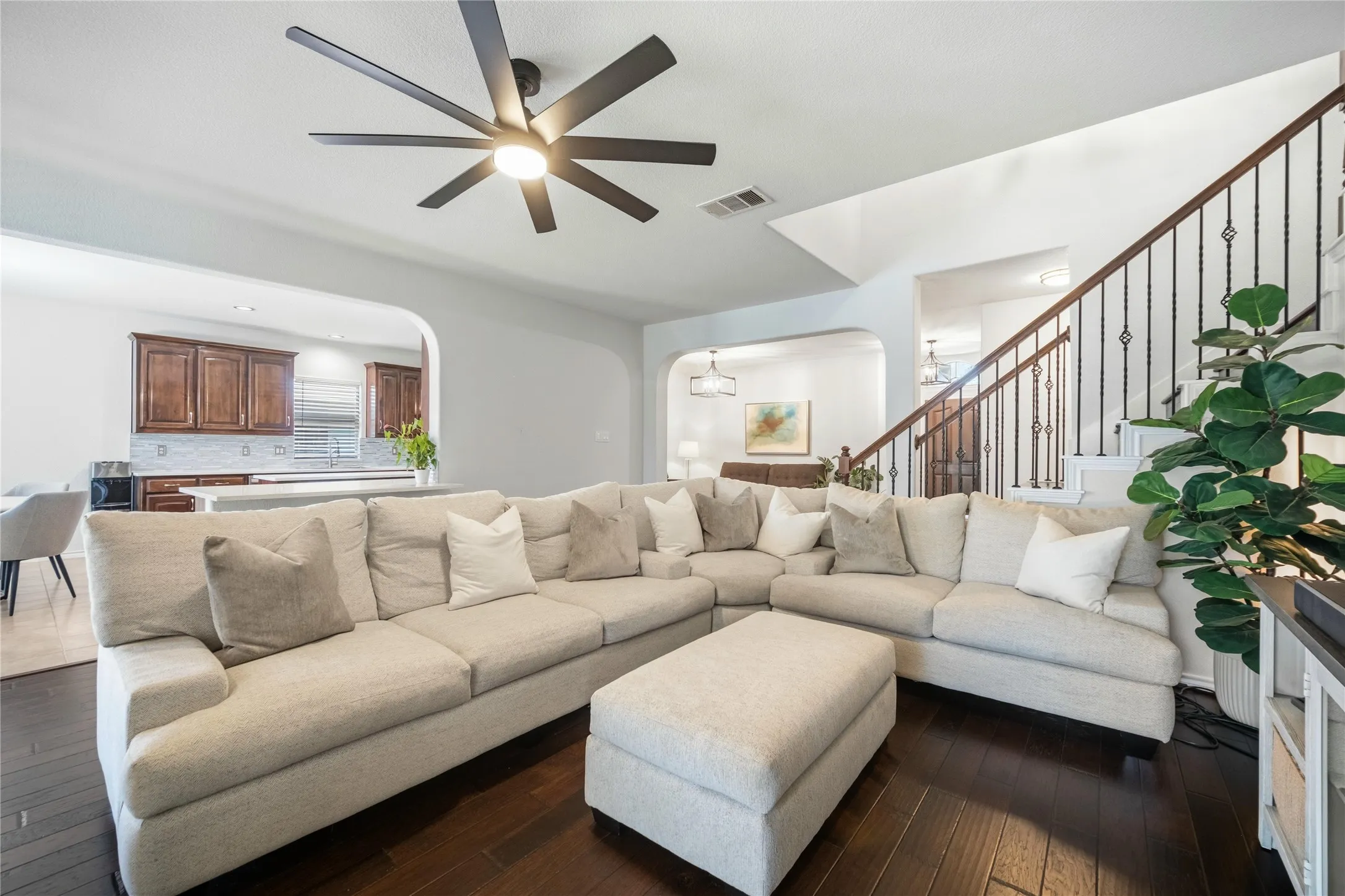 Spacious living area featuring dark wood-finish flooring, a contemporary ceiling fan with light, and an open archway to the kitchen