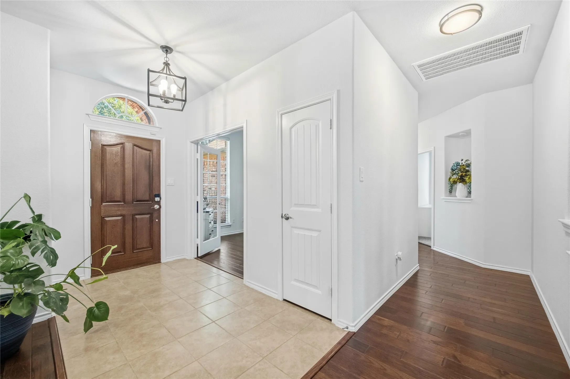 Entryway featuring a rich wood-paneled door with an arched transom window, a decorative pendant light fixture, and tile flooring