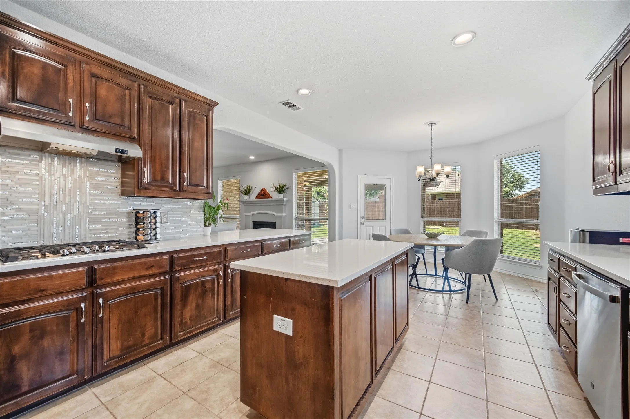 Kitchen featuring rich wood cabinetry, light tile flooring, white countertops, a mosaic tile backsplash, and a central island