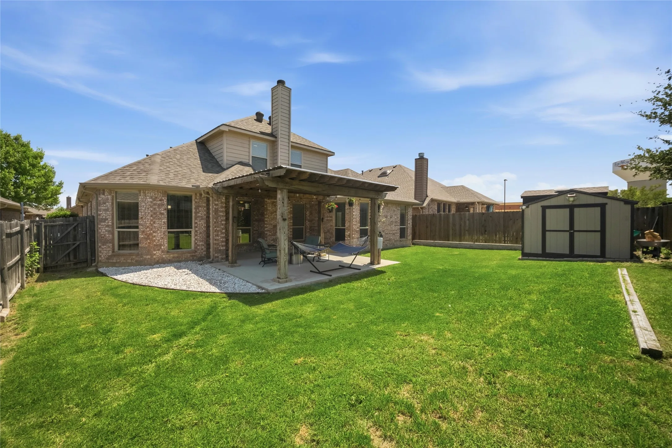 Expansive backyard featuring a covered patio, a detached storage shed, wood privacy fencing, and a stone-lined garden bed