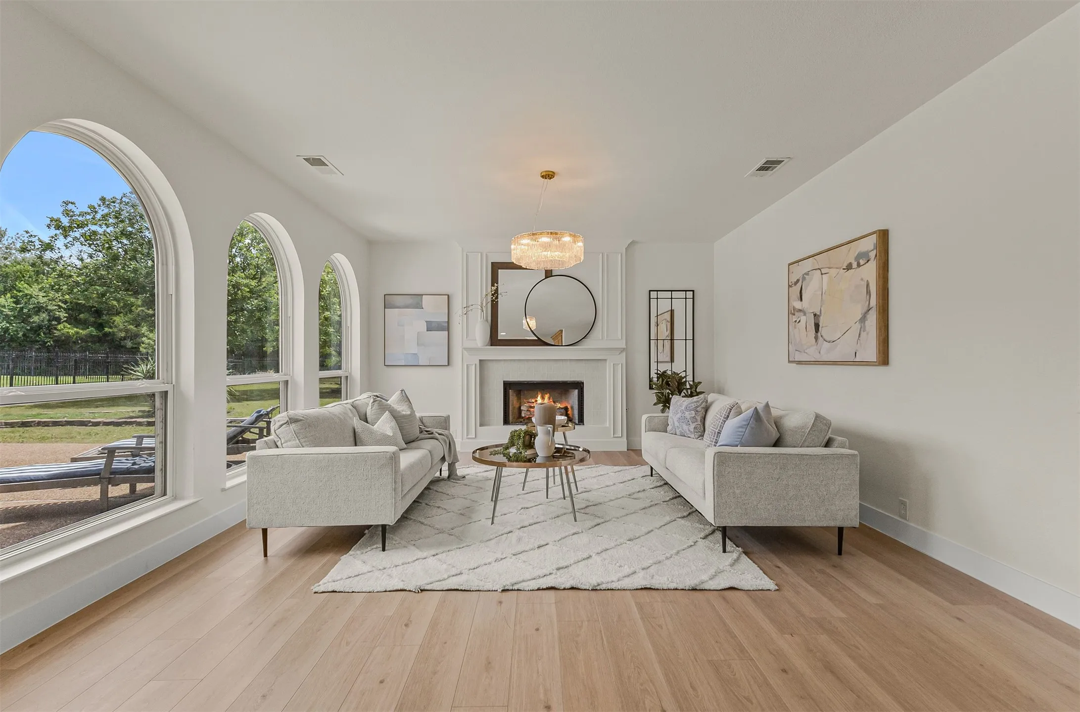 Living area featuring light wood-finish flooring, a white mantel fireplace, three arched windows, a modern chandelier, and recessed lighting