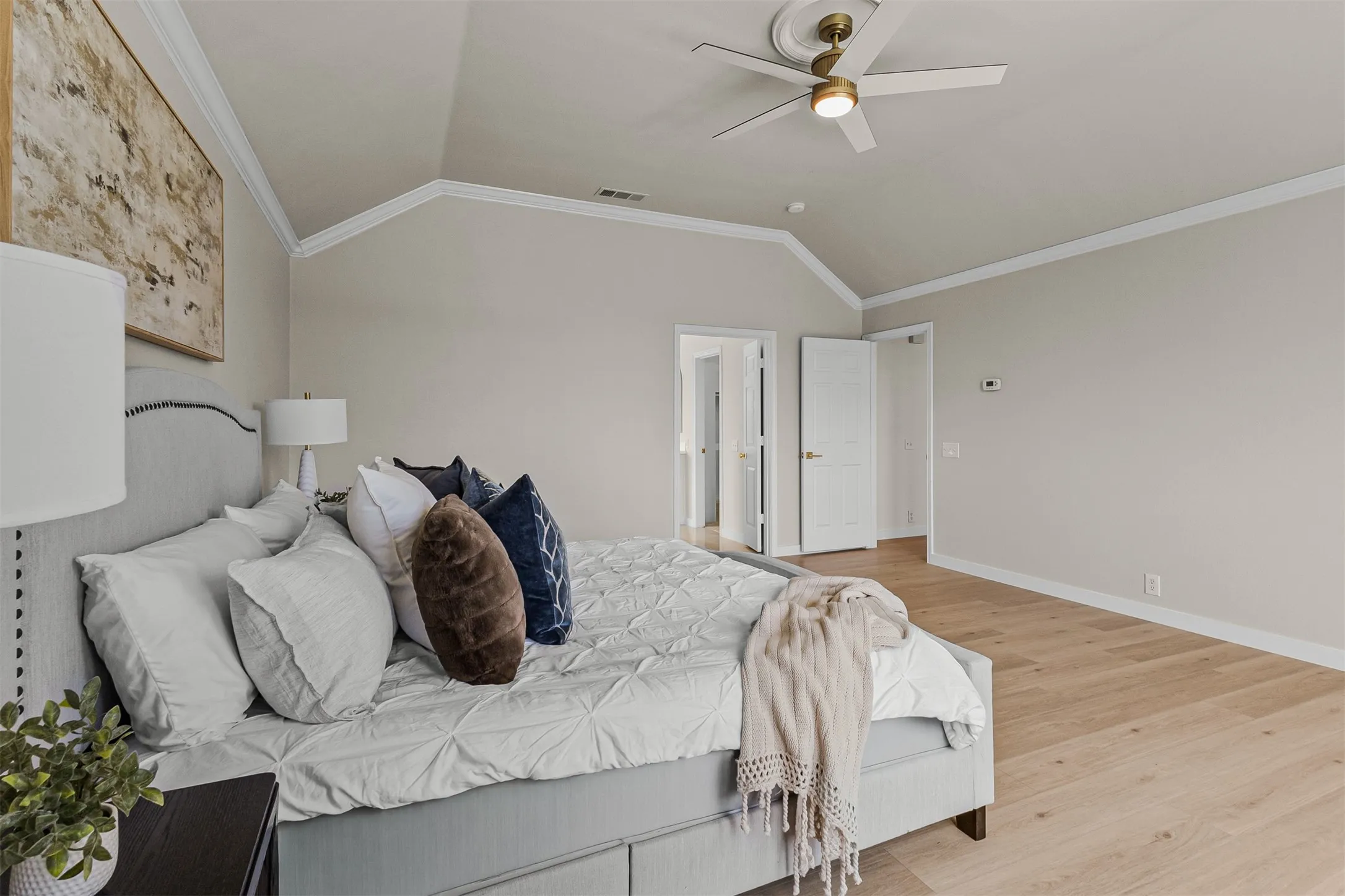 Spacious room featuring vaulted ceilings with crown molding, light wood-finish flooring, and a ceiling fan with integrated lighting