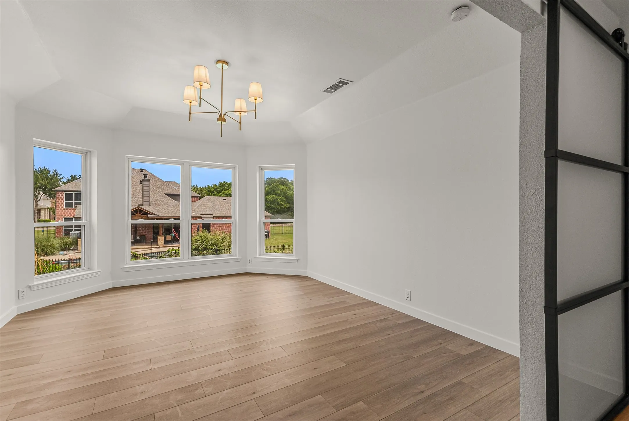 Bay window with multiple large windows, wood-finish flooring, contemporary chandelier, and a modern barn door