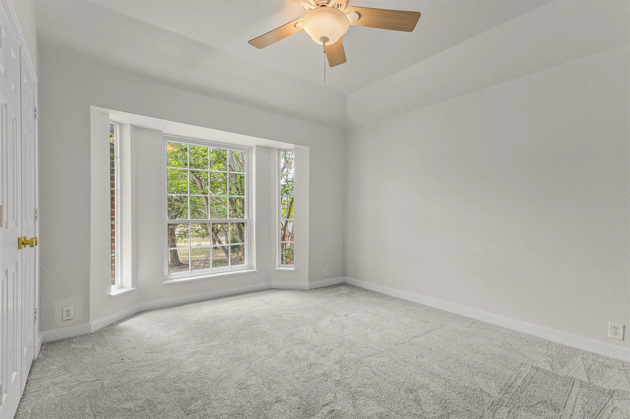 Room featuring a bay window, neutral carpeting, and a ceiling fan with light fixture