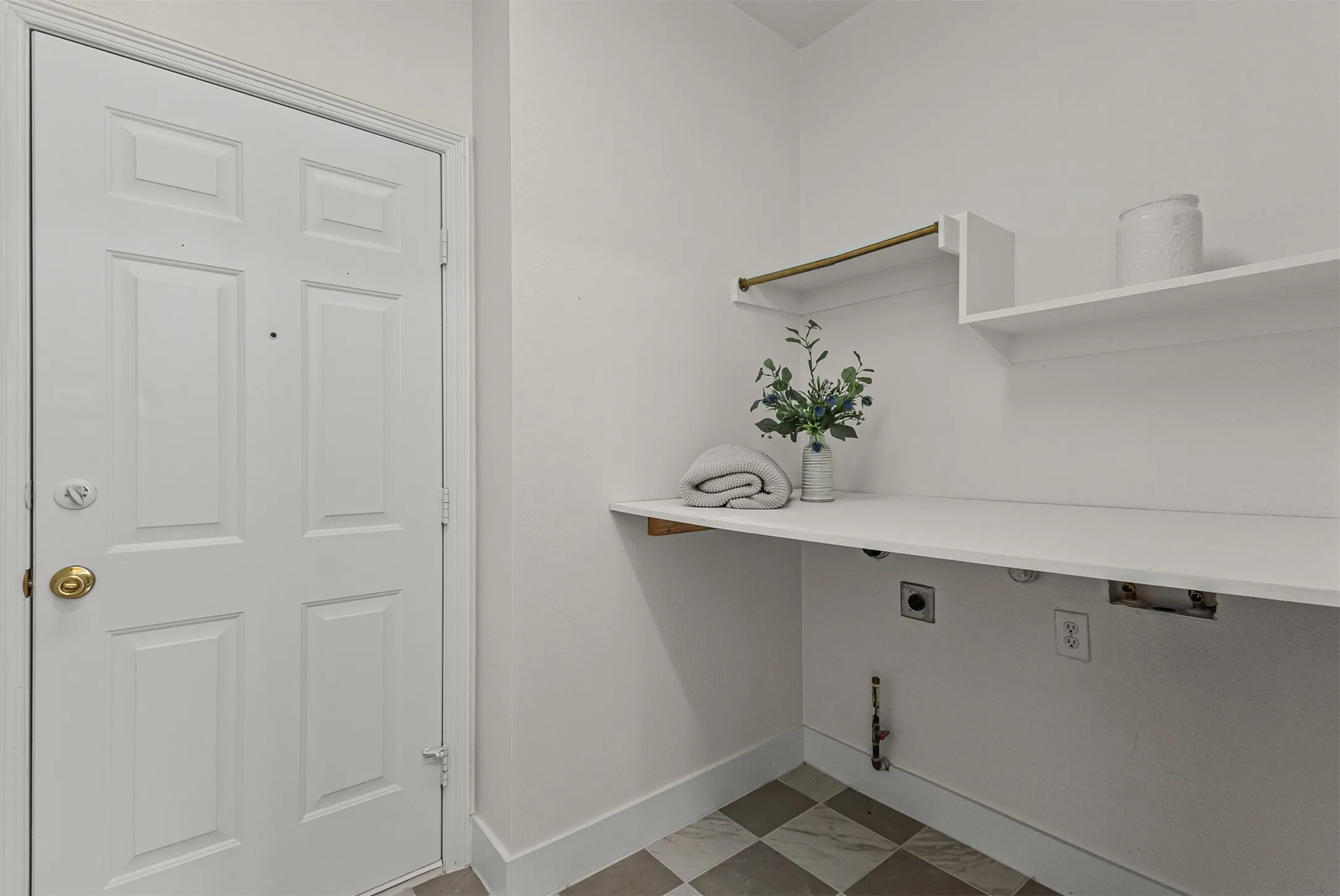 Dedicated utility area featuring white paneled door, built-in shelving, hanging rod, extensive countertop space, and checkered floor tile