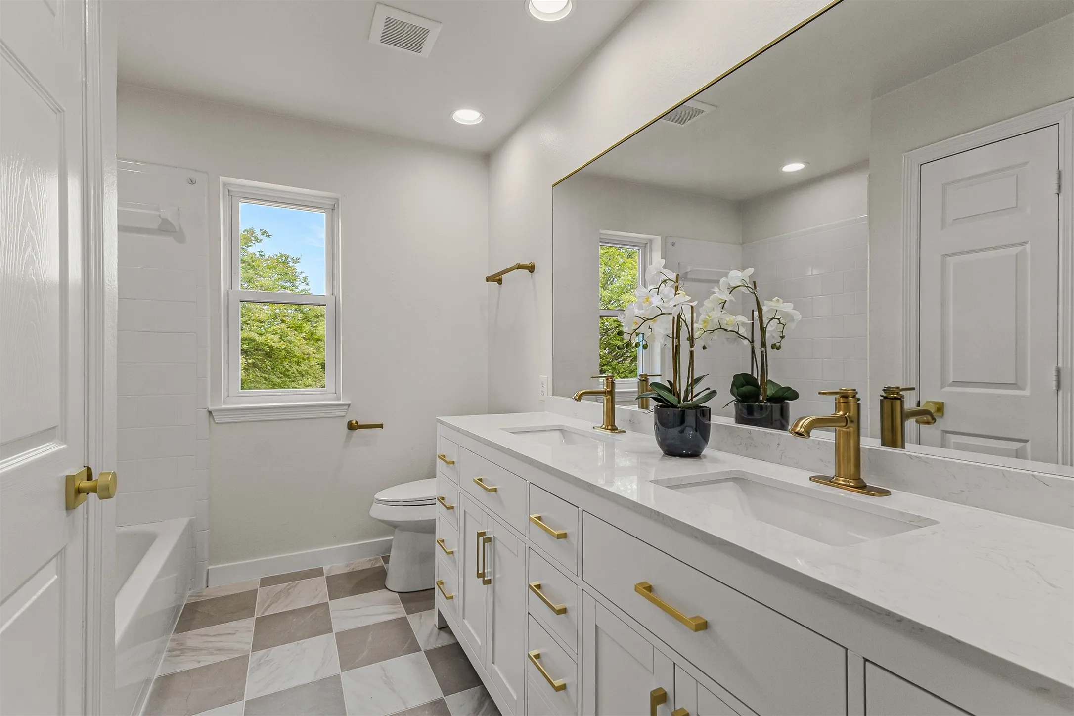 White shaker-style double vanity with integrated sinks, light-toned countertop, and gold-finish fixtures