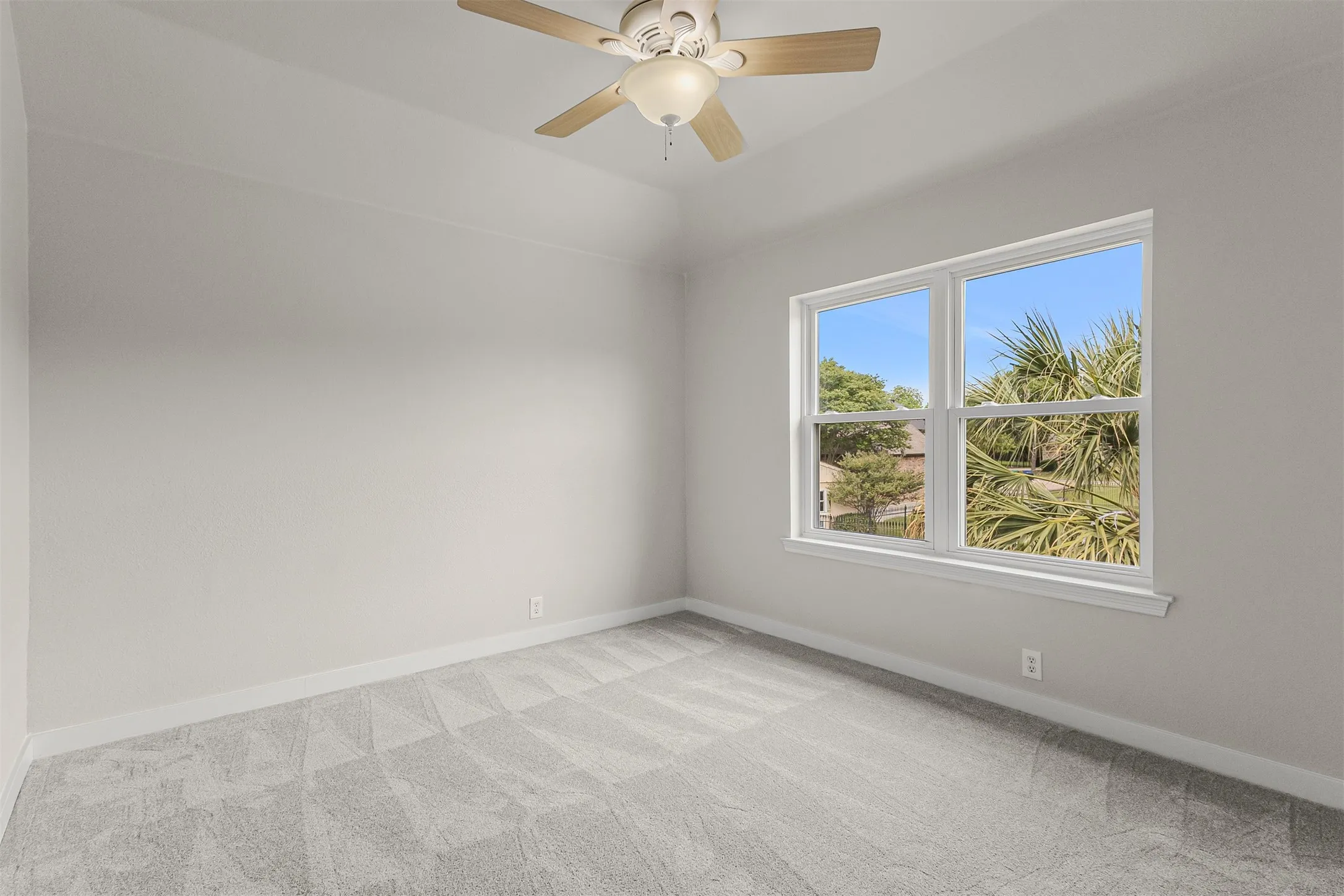 Room featuring a neutral gray carpet and walls, a window offering natural light, white window trim, and a ceiling fan with light fixture