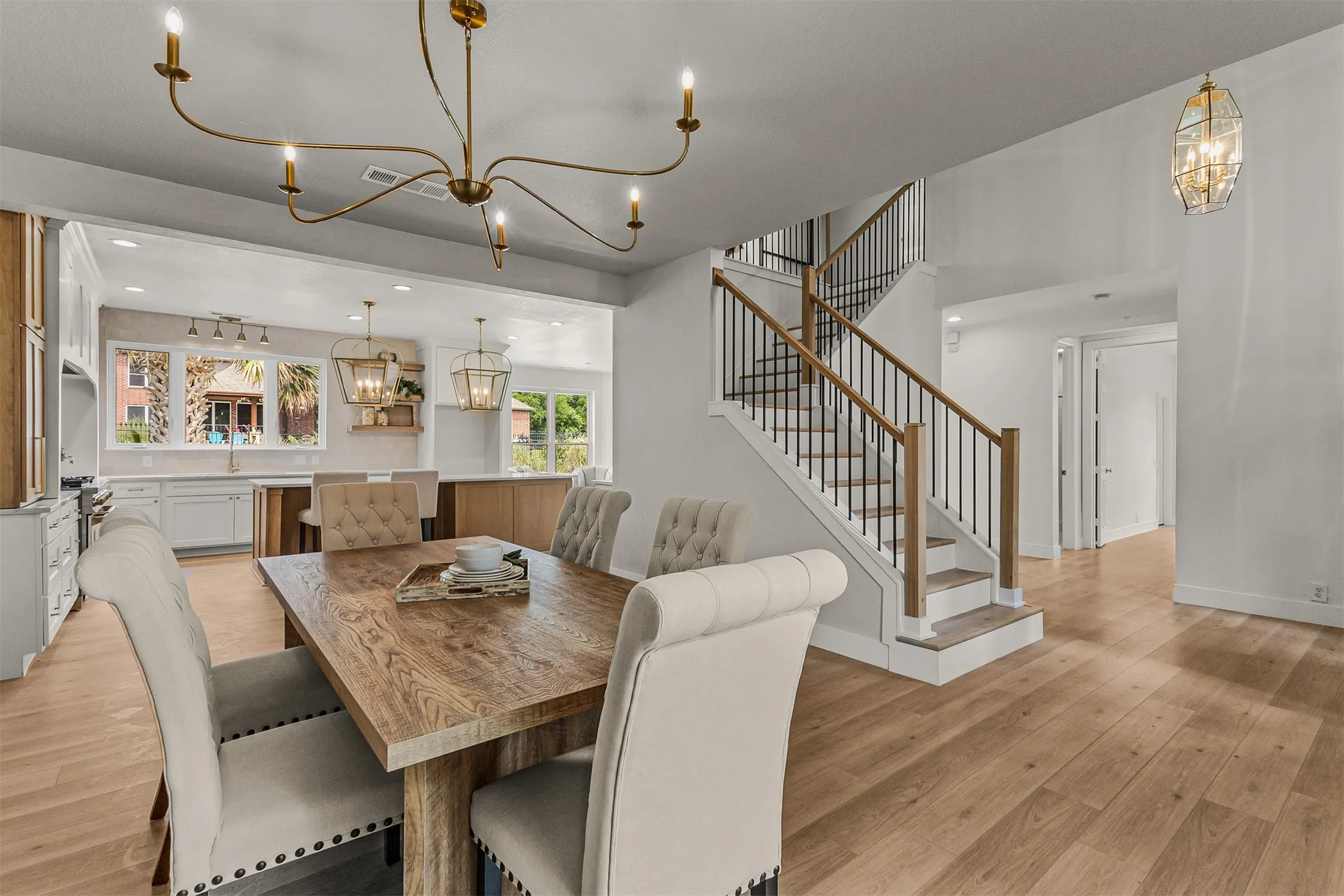 Open-concept interior featuring light wood-finish flooring throughout, a white kitchen with a light-colored countertop and island, and a staircase with a wood handrail and black iron balusters