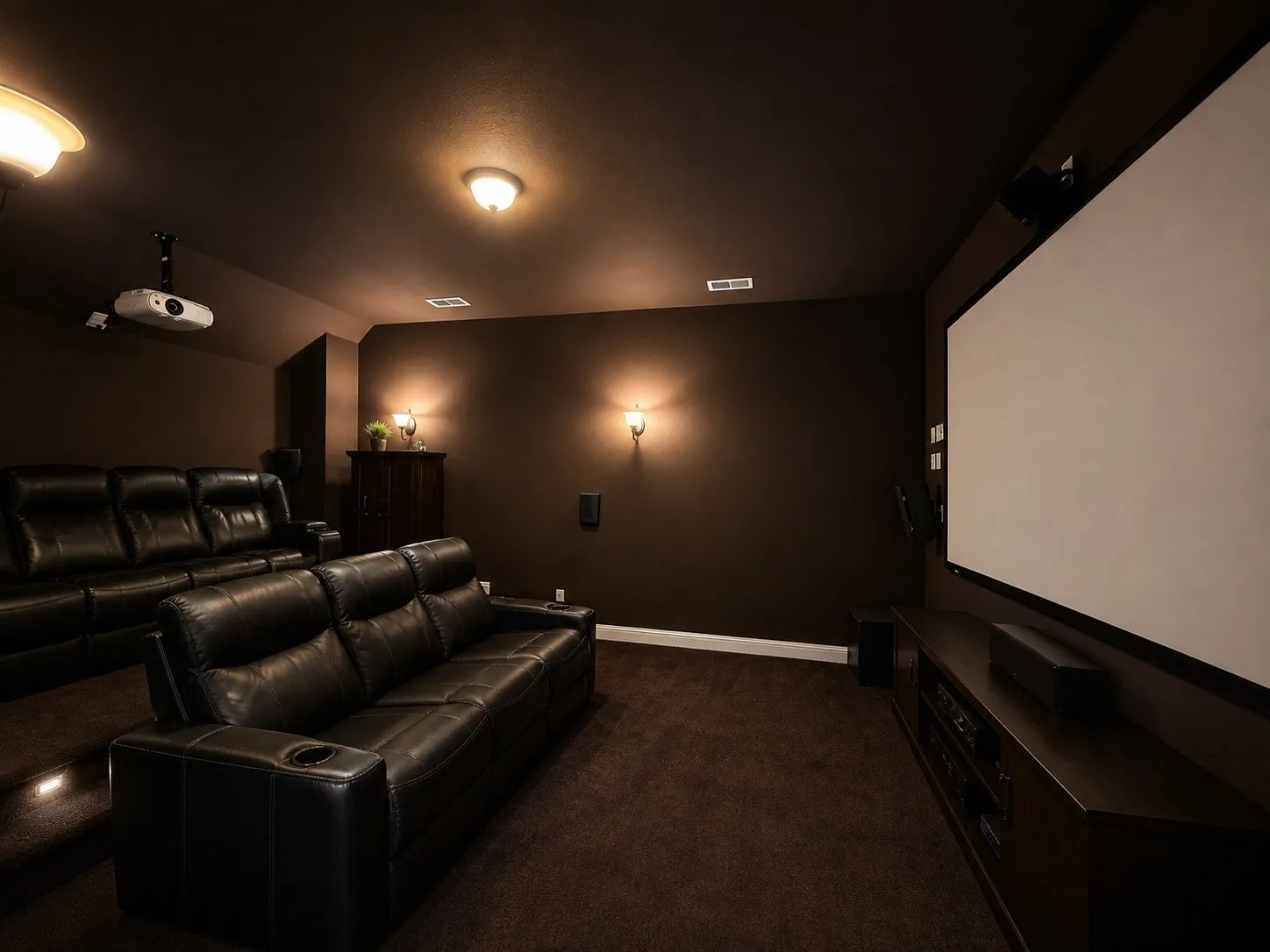Dedicated entertainment space featuring a large projection screen, mounted projector, built-in speakers, wall sconces, and layered brown carpeting