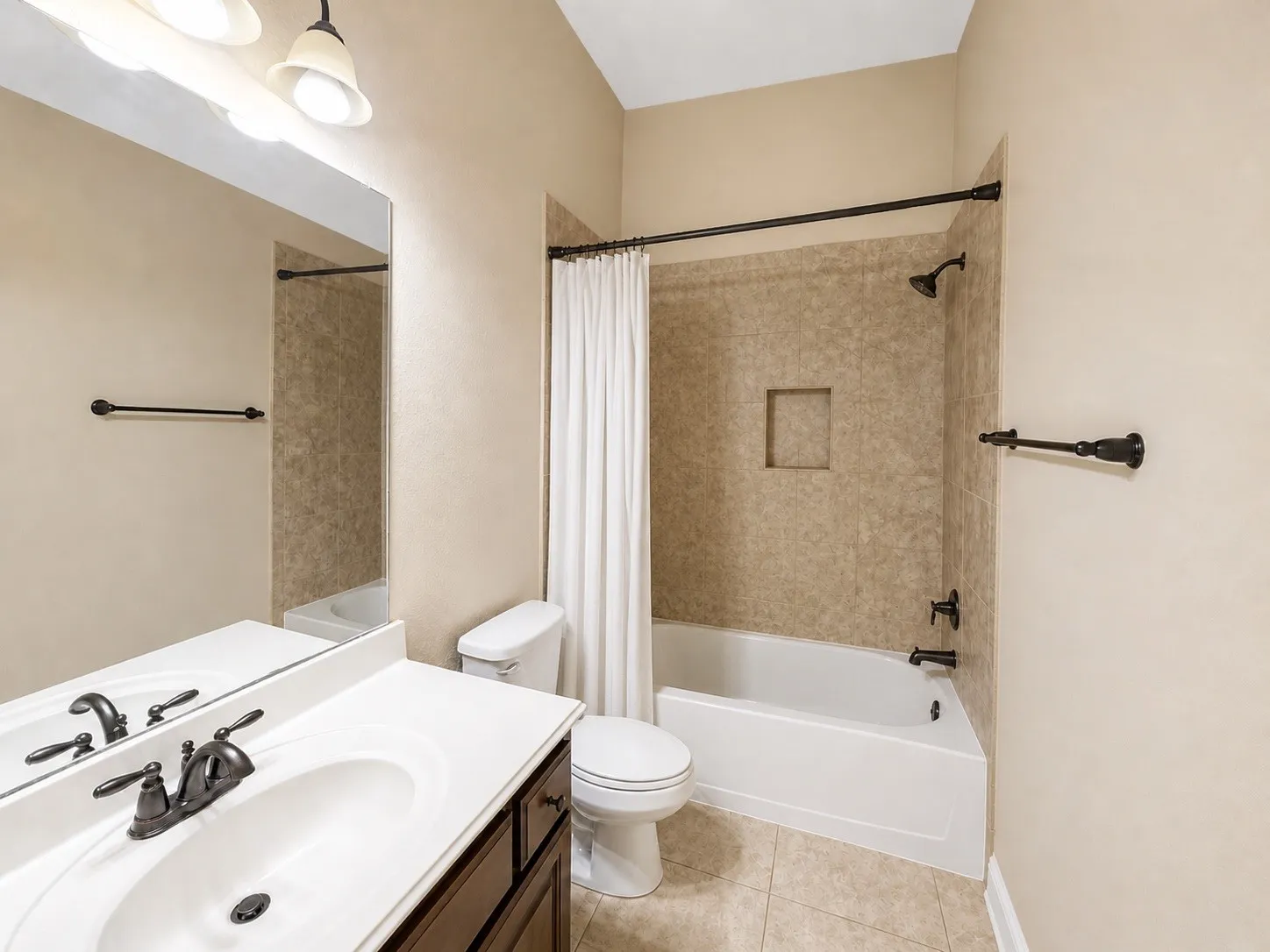 Bathroom featuring a white vanity with an integrated sink, dark bronze fixtures, and an expansive wall mirror