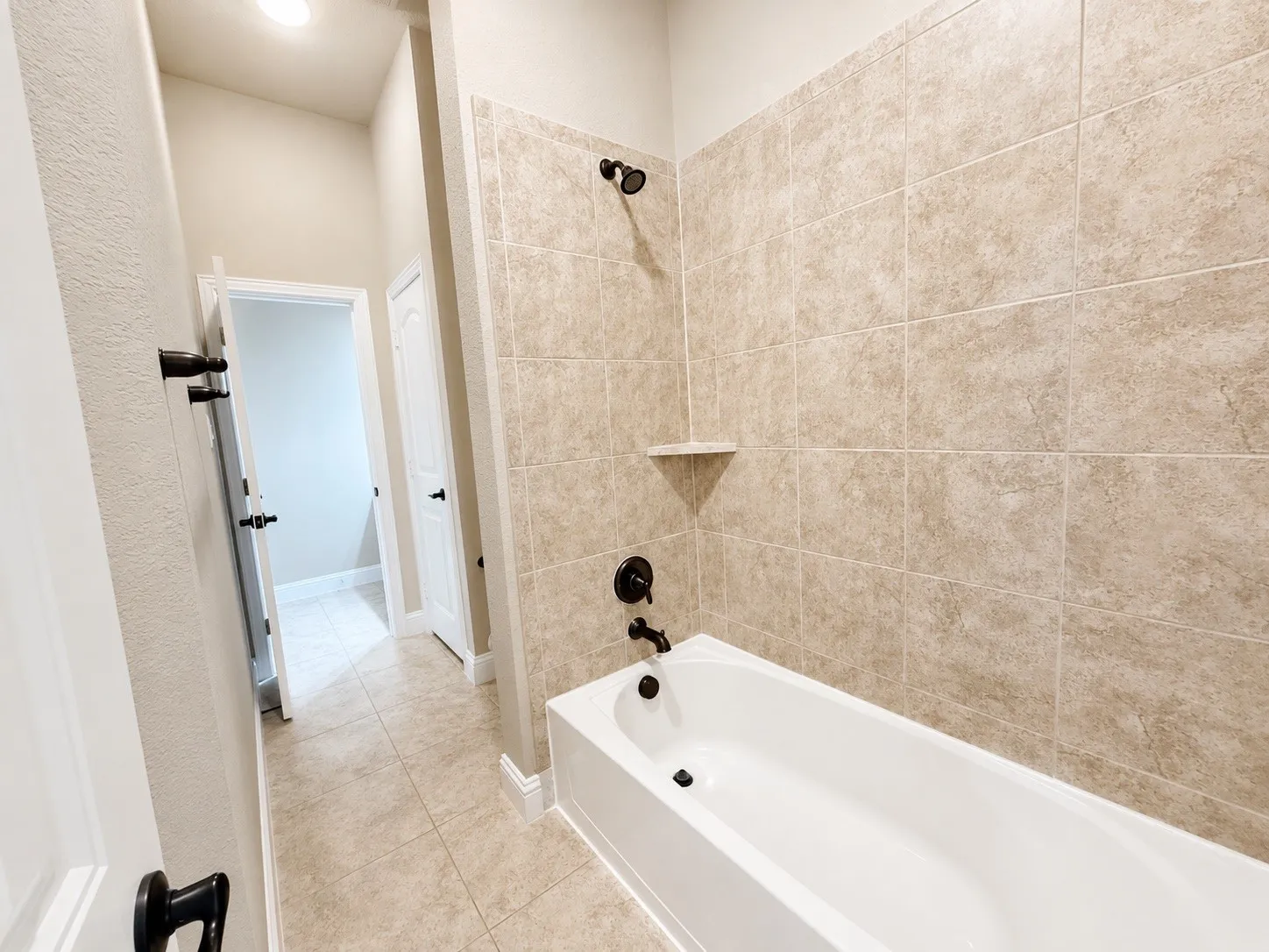 Bathtub and shower combination featuring neutral-toned tile surround, matte black fixtures, and an integrated corner shelf