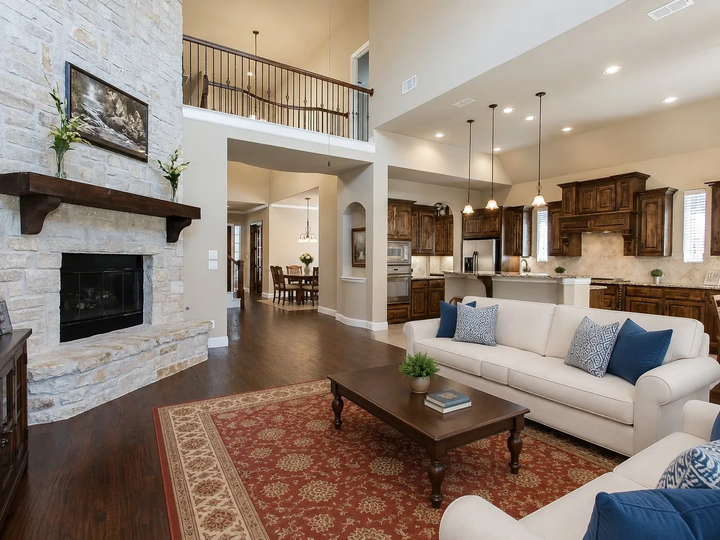 Two-story living area with a stone fireplace, wood-finish flooring, and an upper-level balcony
