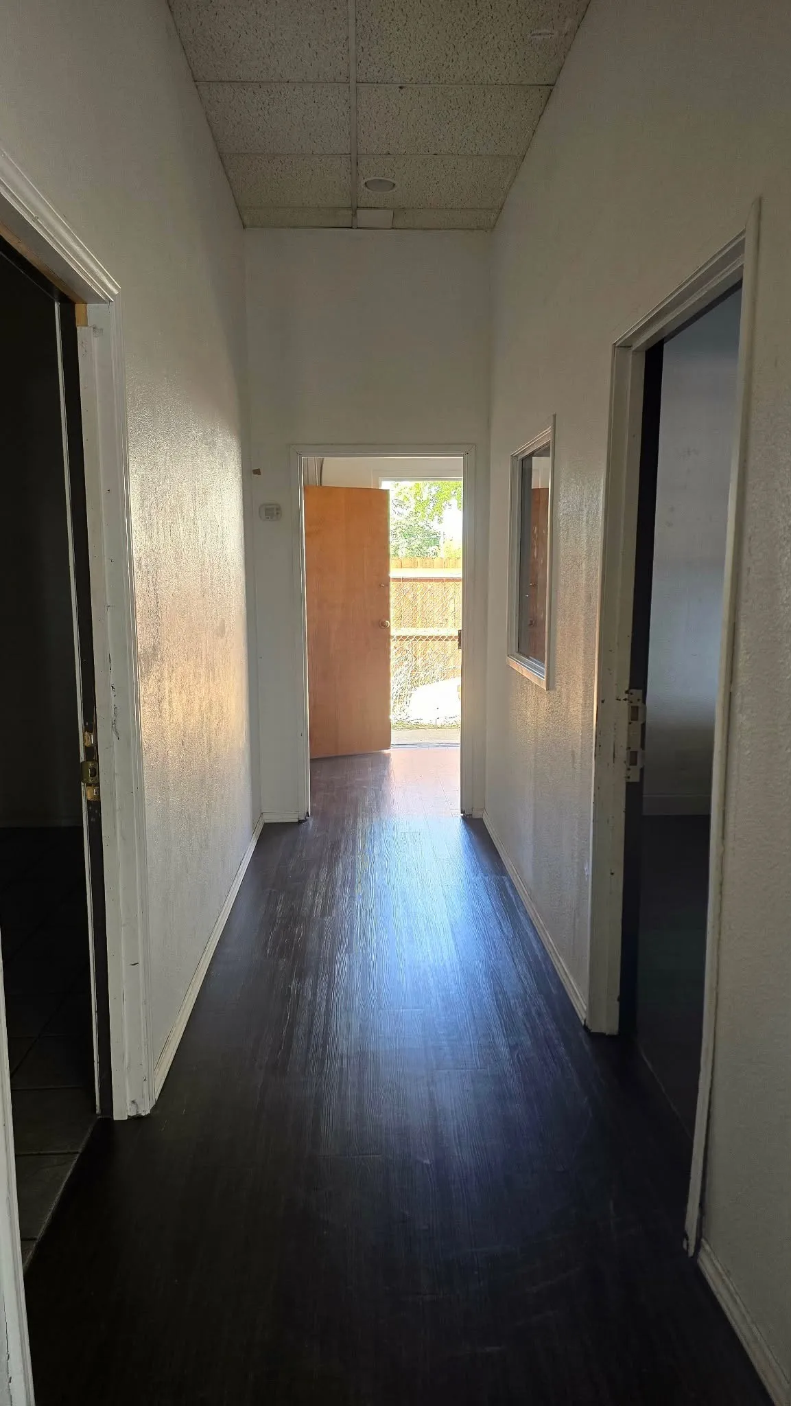 Hallway with dark wood-finish flooring, white walls, and a drop-tile ceiling