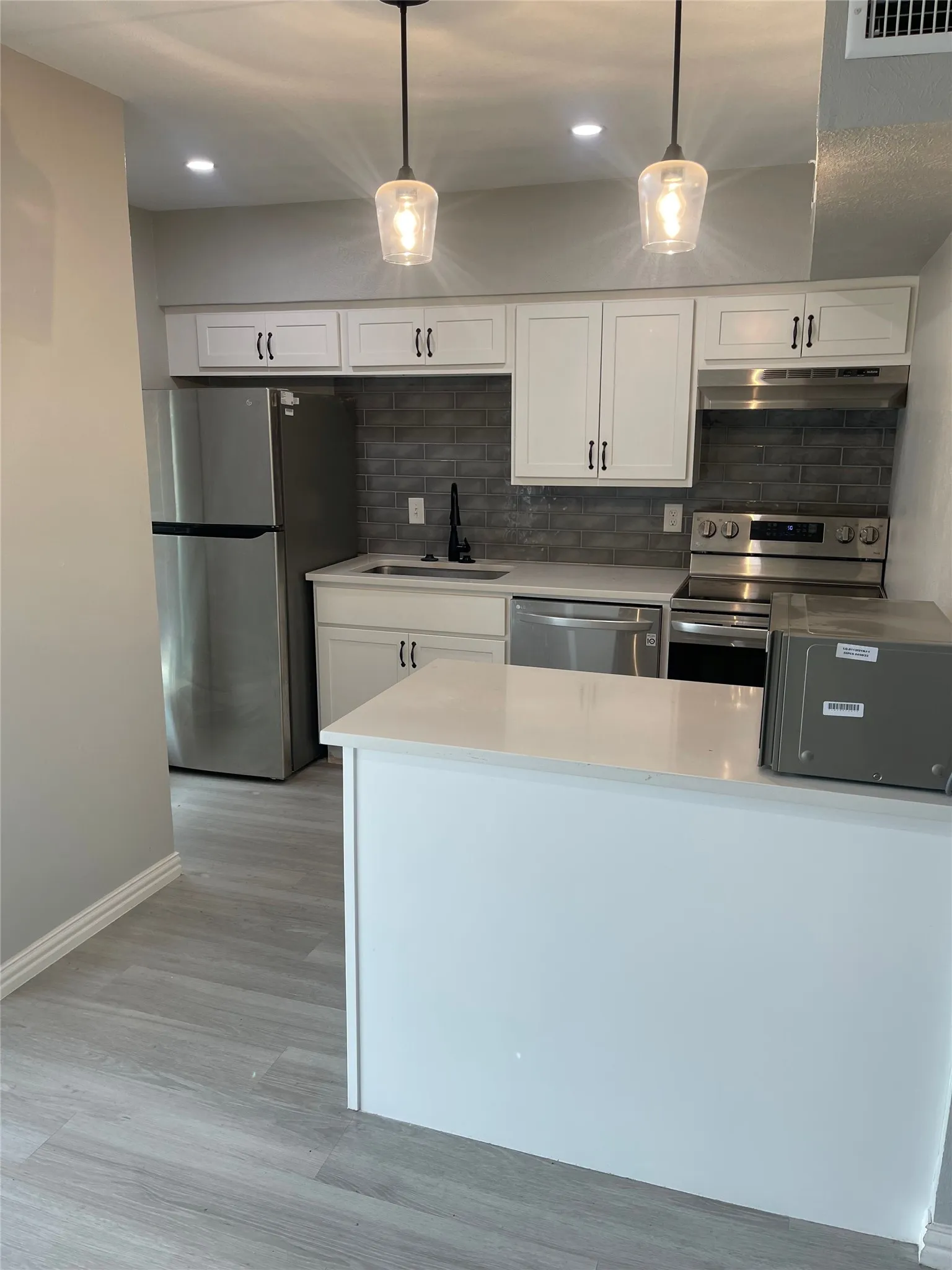 Modern kitchen featuring white cabinetry with dark hardware, stainless steel appliances, a dark subway tile backsplash, light countertops, and wood-finish flooring