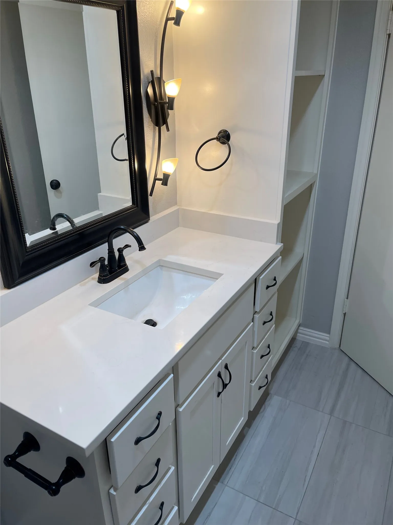 Contemporary bathroom vanity featuring a rectangular undermount sink, solid surface countertop, and white cabinetry with black hardware