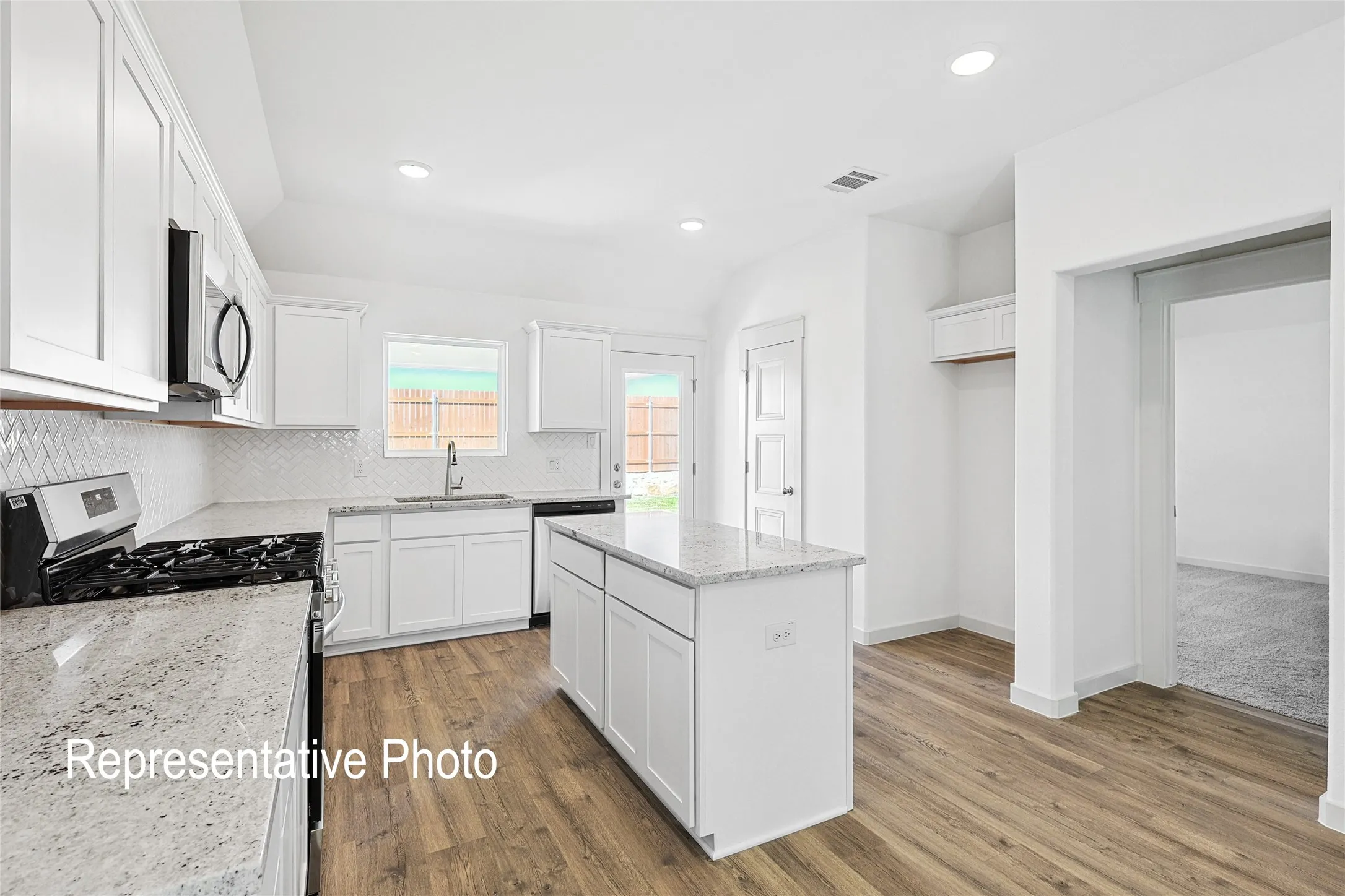 Modern kitchen featuring white cabinetry, granite countertops, an island with storage, wood-finish flooring, and stainless steel appliances