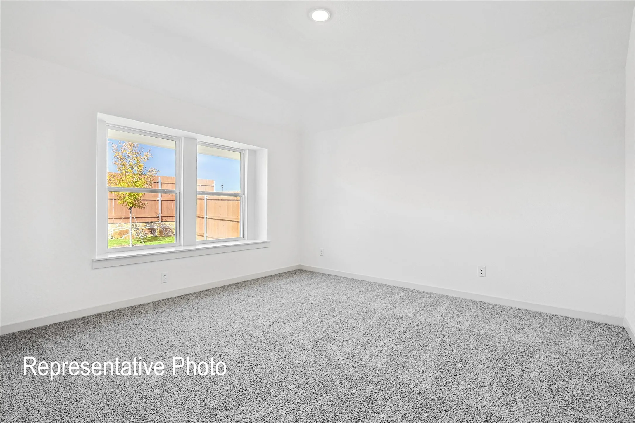 Spacious room featuring neutral carpeting, white walls, a recessed ceiling light, and a large window providing ample ambient light