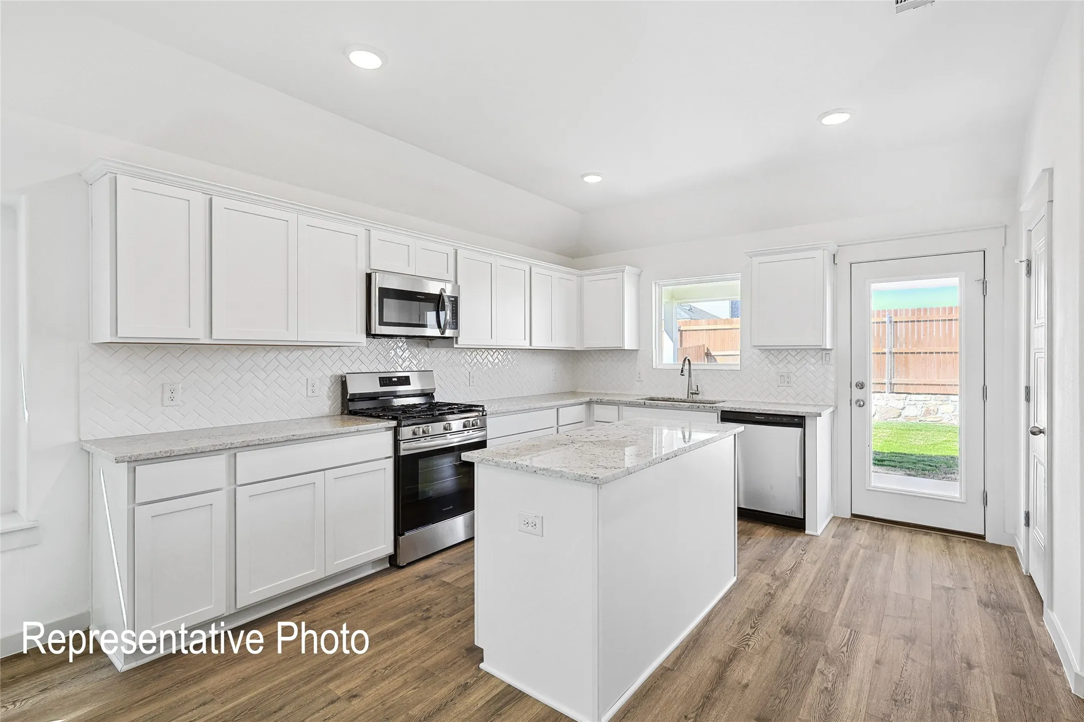 Bright kitchen featuring white cabinetry, stainless steel appliances, a white tile backsplash, and a central island with a stone-finish countertop