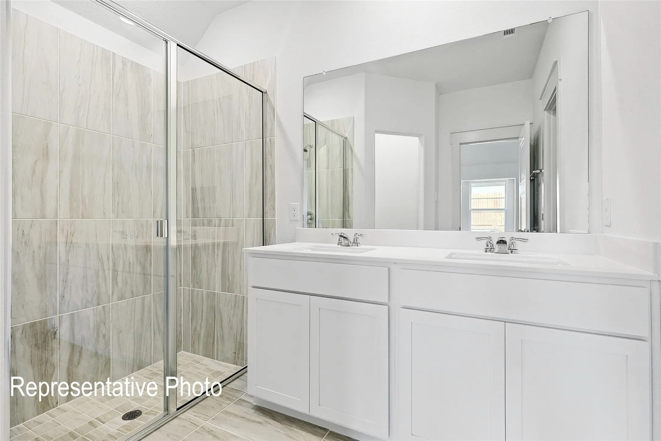 Modern bathroom featuring a double vanity with white cabinetry and integrated sinks, a wide wall-mounted mirror, and a glass-enclosed shower with vertical tile work
