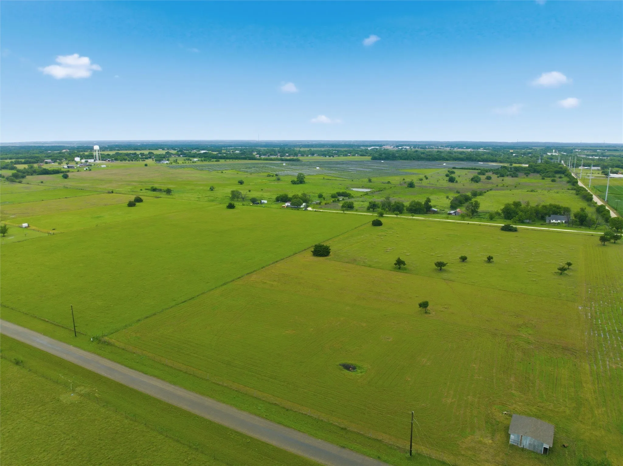 Expansive green acreage with scattered trees and a paved road