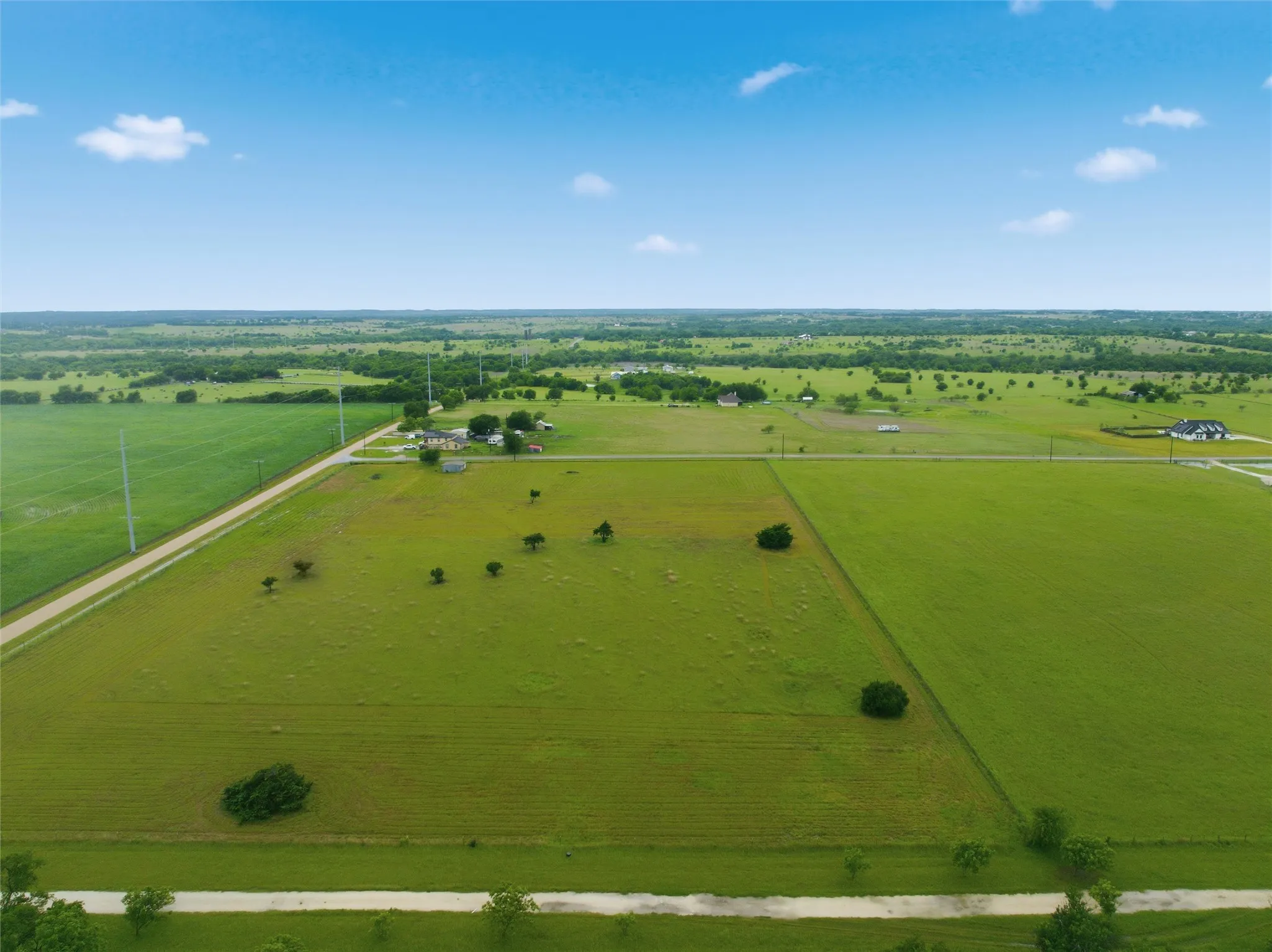 Expansive green fields with scattered mature trees and visible utility poles