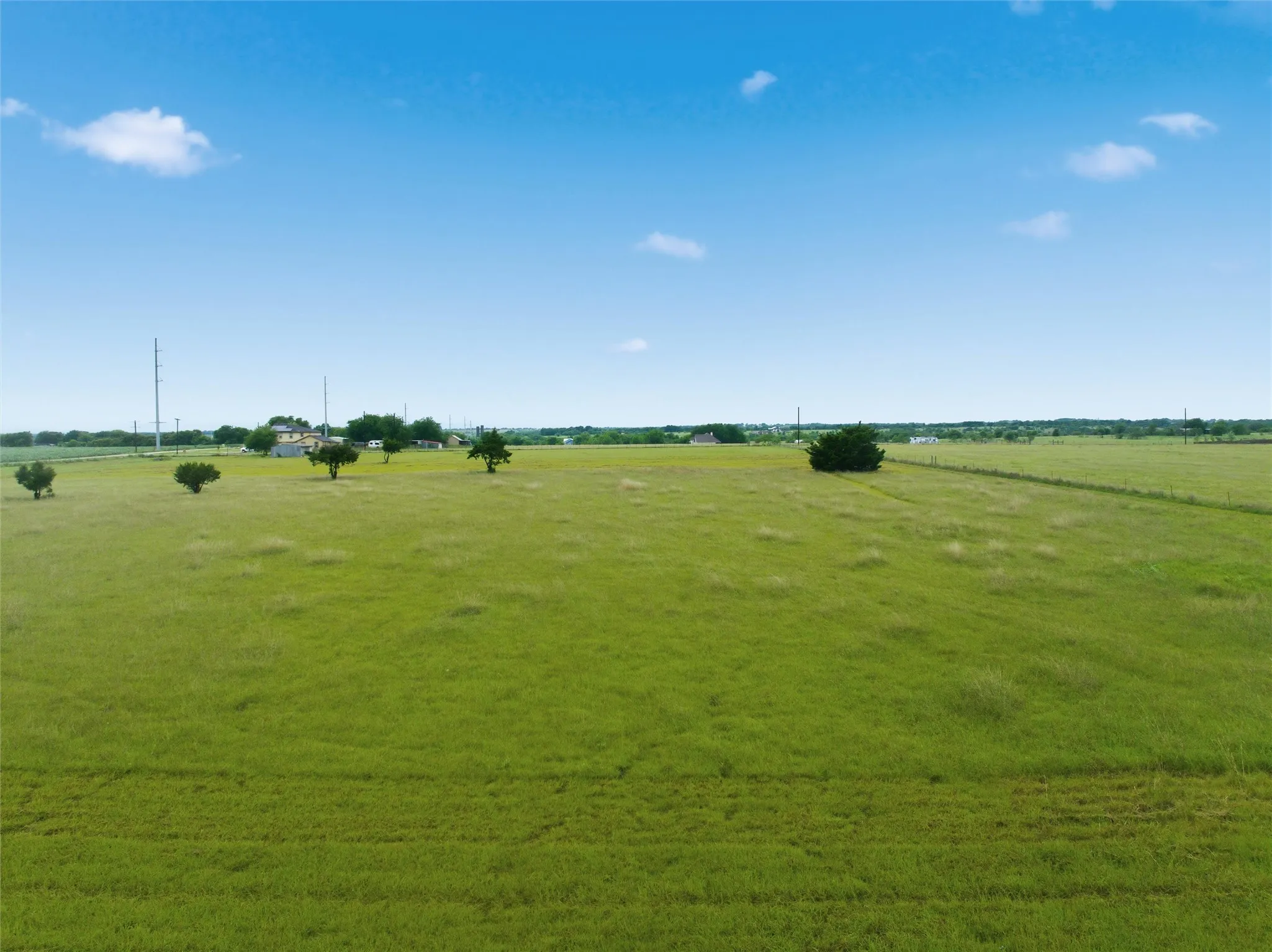 Expansive green land area featuring scattered trees and distant structures