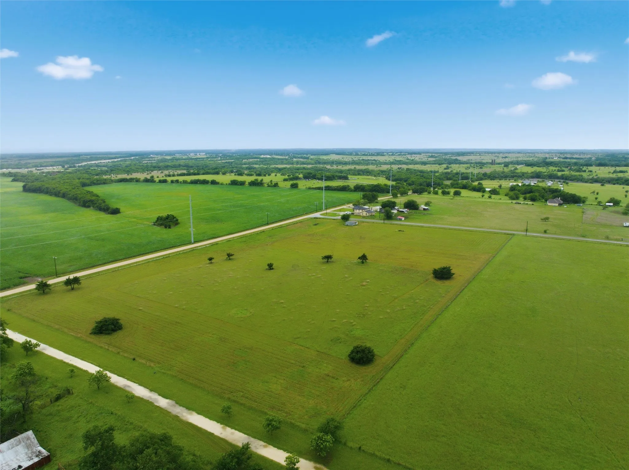 Expansive rural property featuring multiple green pastures, scattered mature trees, and visible clear sky