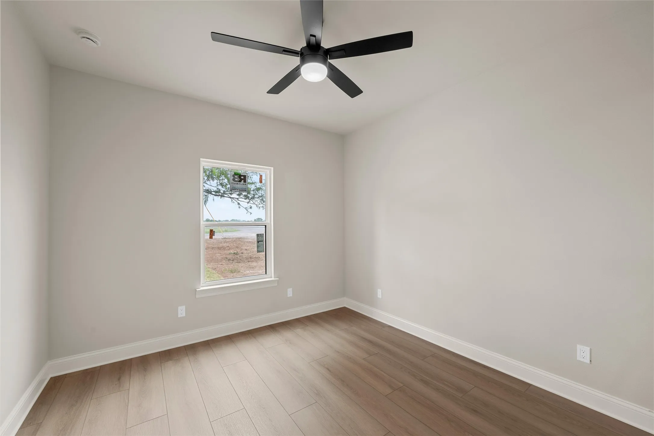 Neutral tone walls with white trim, wood-finish flooring, and a modern black ceiling fan with integrated lighting