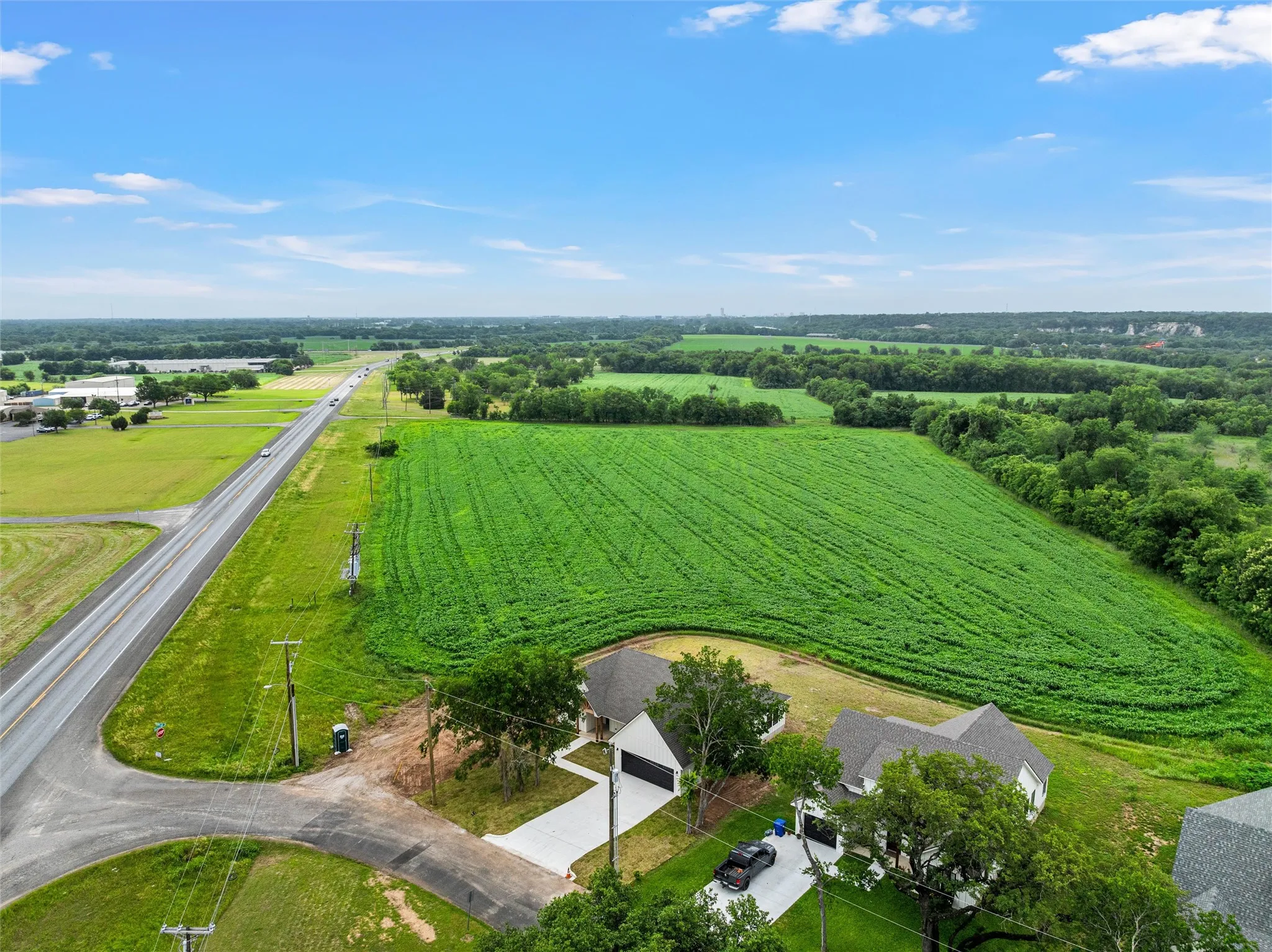 Expansive green acreage with a paved road frontage, bordering cultivated fields and mature tree lines