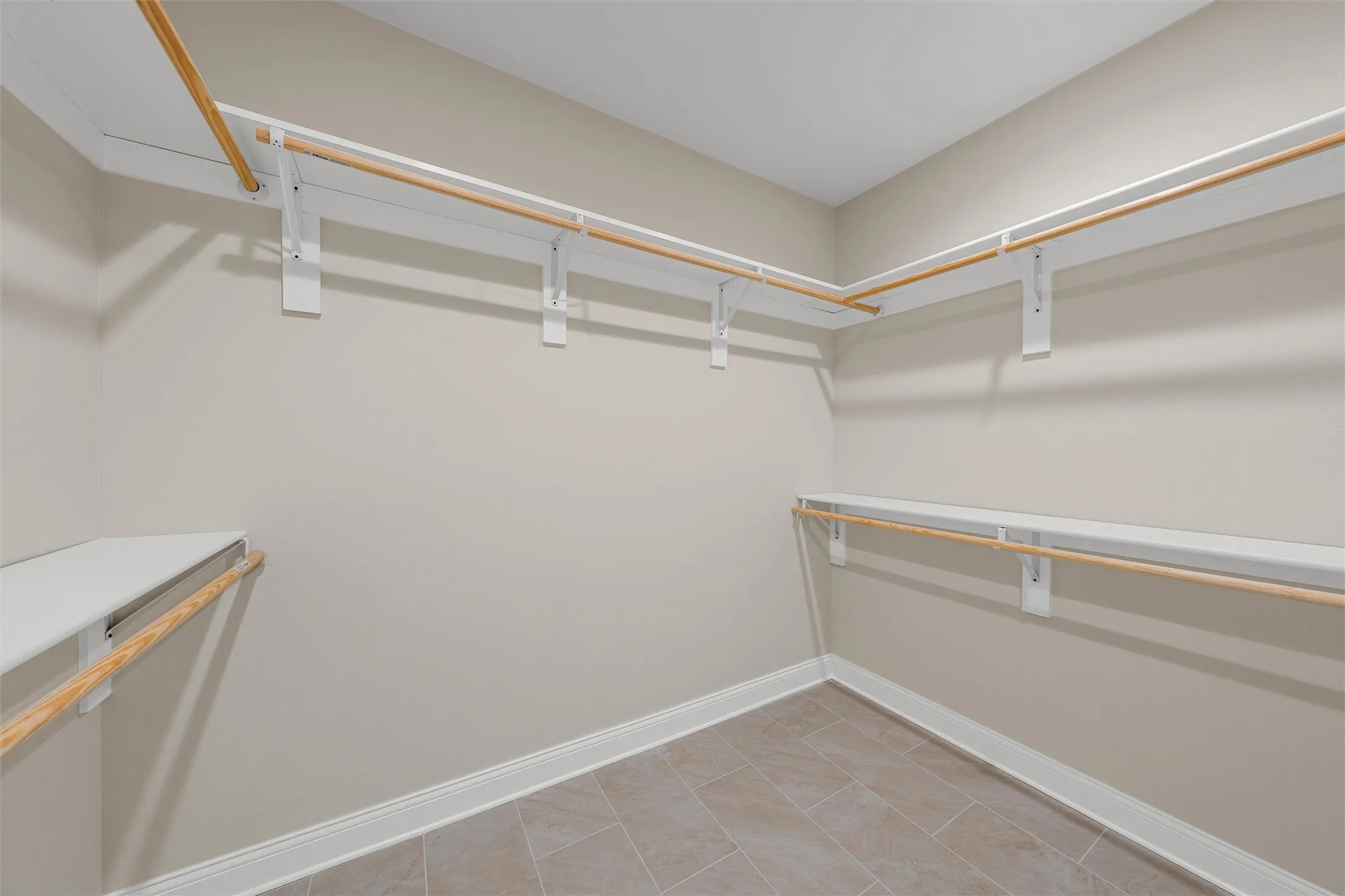 Walk-in closet featuring light beige wall paint, white baseboards, and neutral-toned rectangular floor tiles