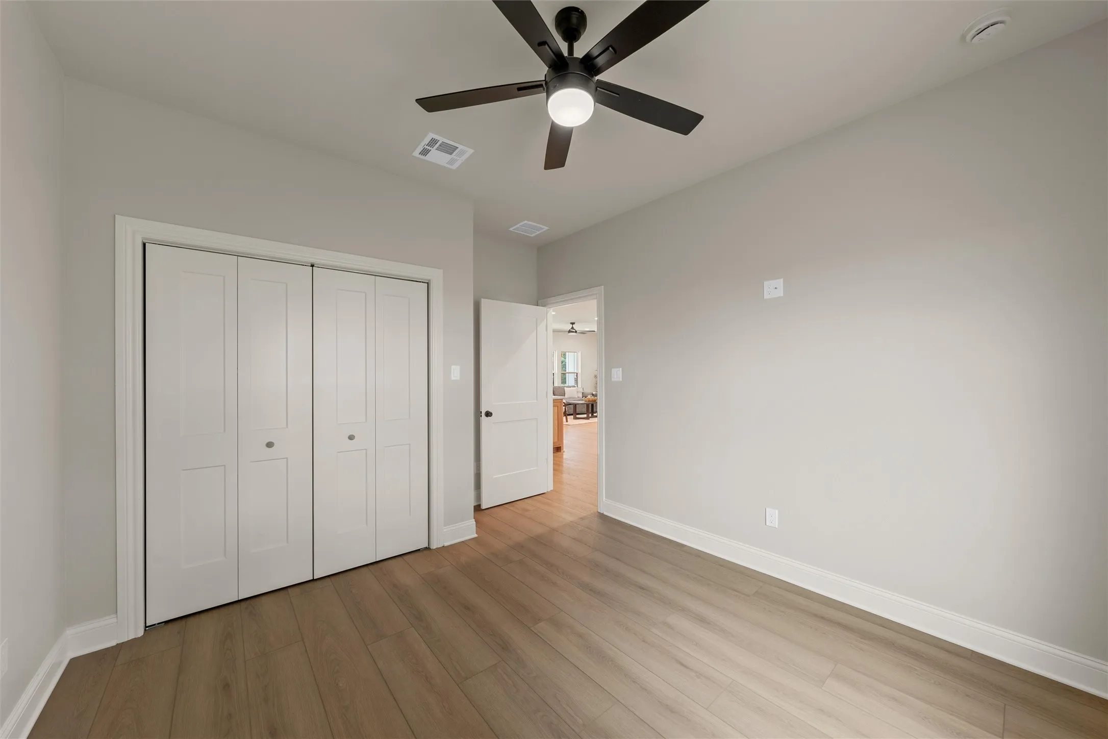 Spacious room featuring wood-finish flooring, light gray wall paint, and a dark-toned ceiling fan with integrated lighting