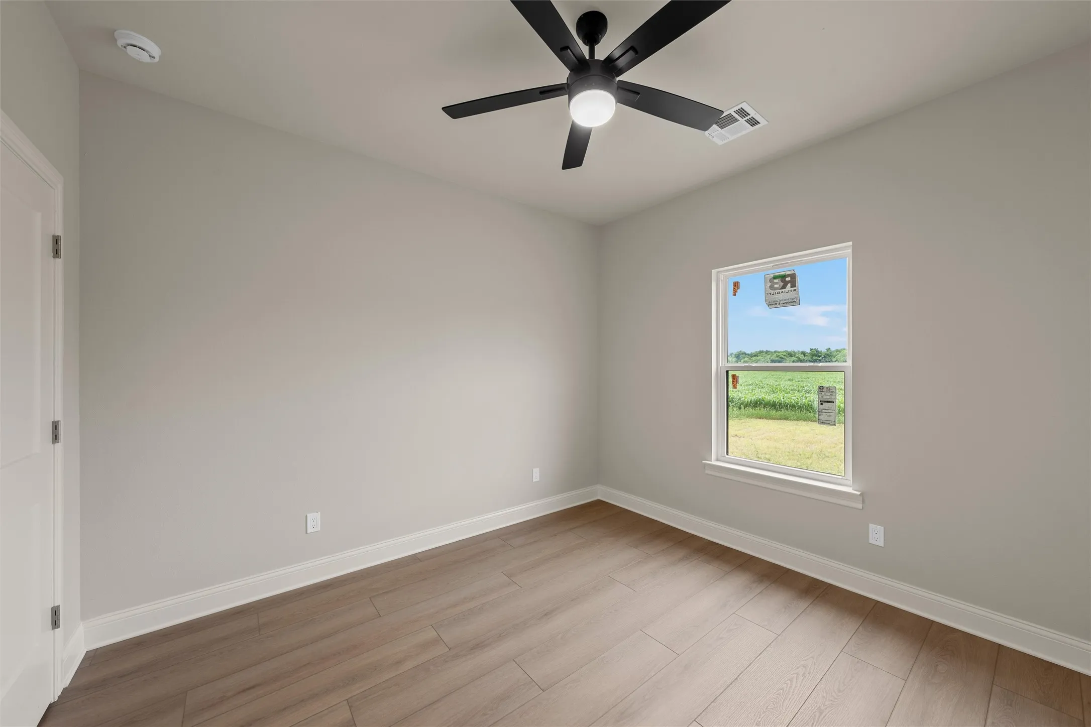 Room featuring wood-finish flooring, a contemporary ceiling fan with integrated lighting, and a single window with white trim