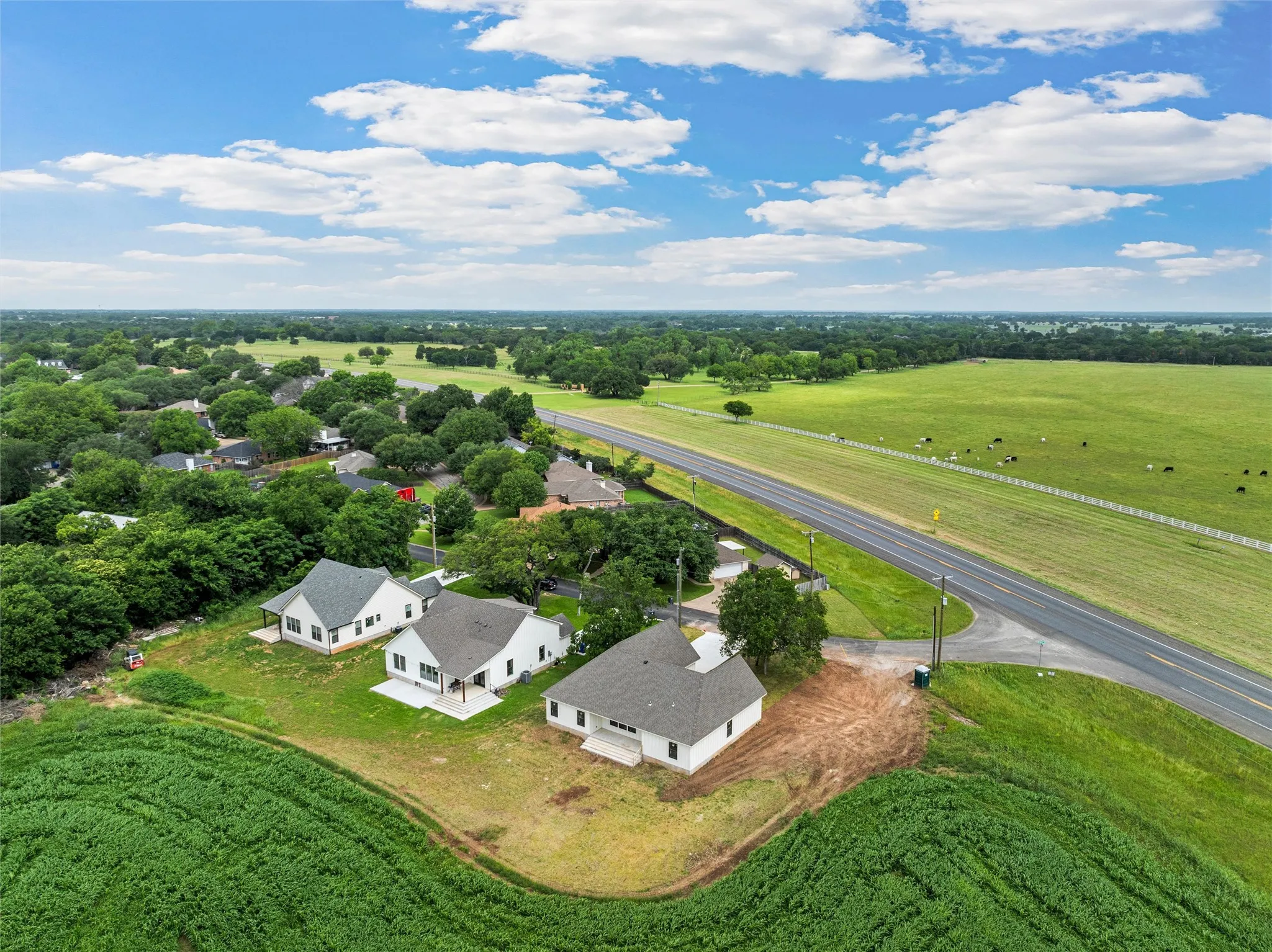 Aerial perspective showcasing multiple properties, green fields, and a paved road
