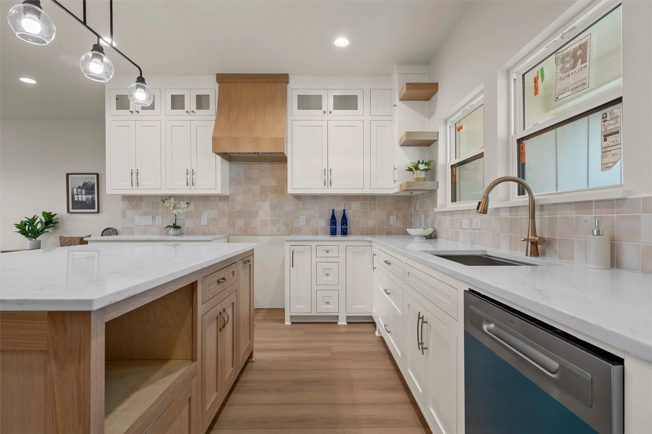 Kitchen featuring white upper and lower cabinetry, a natural wood-finish island with a light-toned countertop, a stainless steel dishwasher, a single basin sink with a curved faucet, and wood-finish flooring