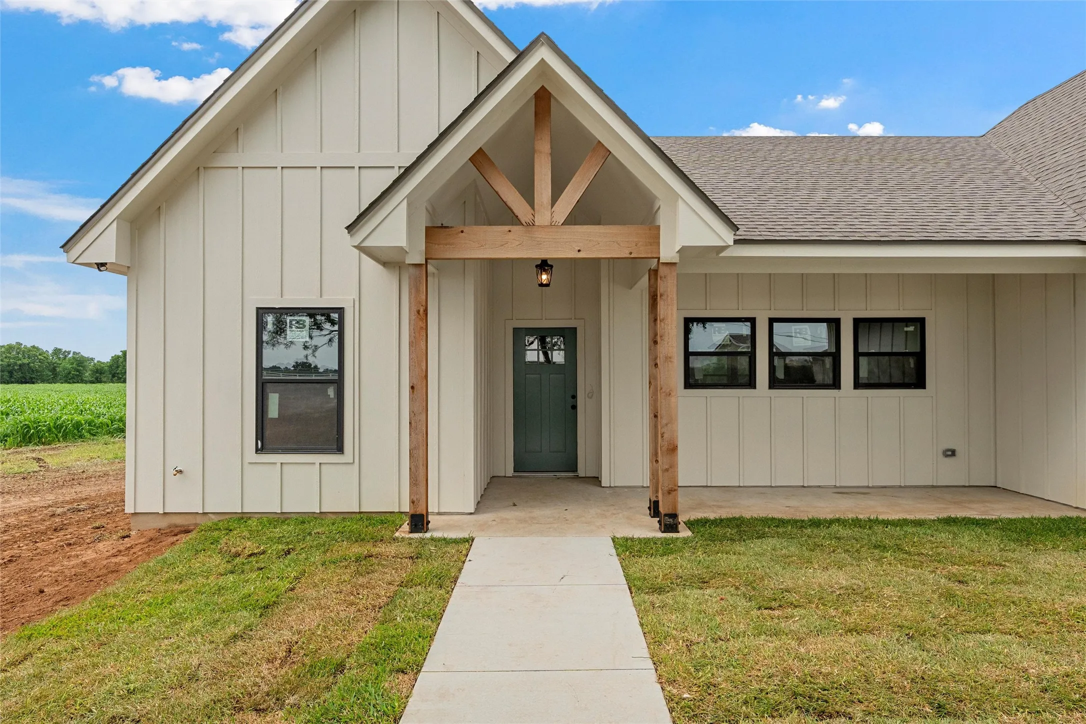 Modern farmhouse exterior featuring board and batten siding, a covered entry with timber frame accents, a dark green entry door, black-framed windows, and a concrete walkway