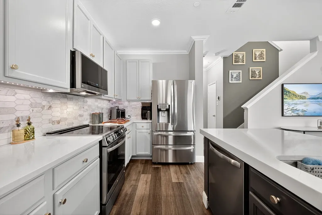 Contemporary kitchen featuring stainless steel appliances, white cabinetry, solid surface countertops, and wood-finish flooring