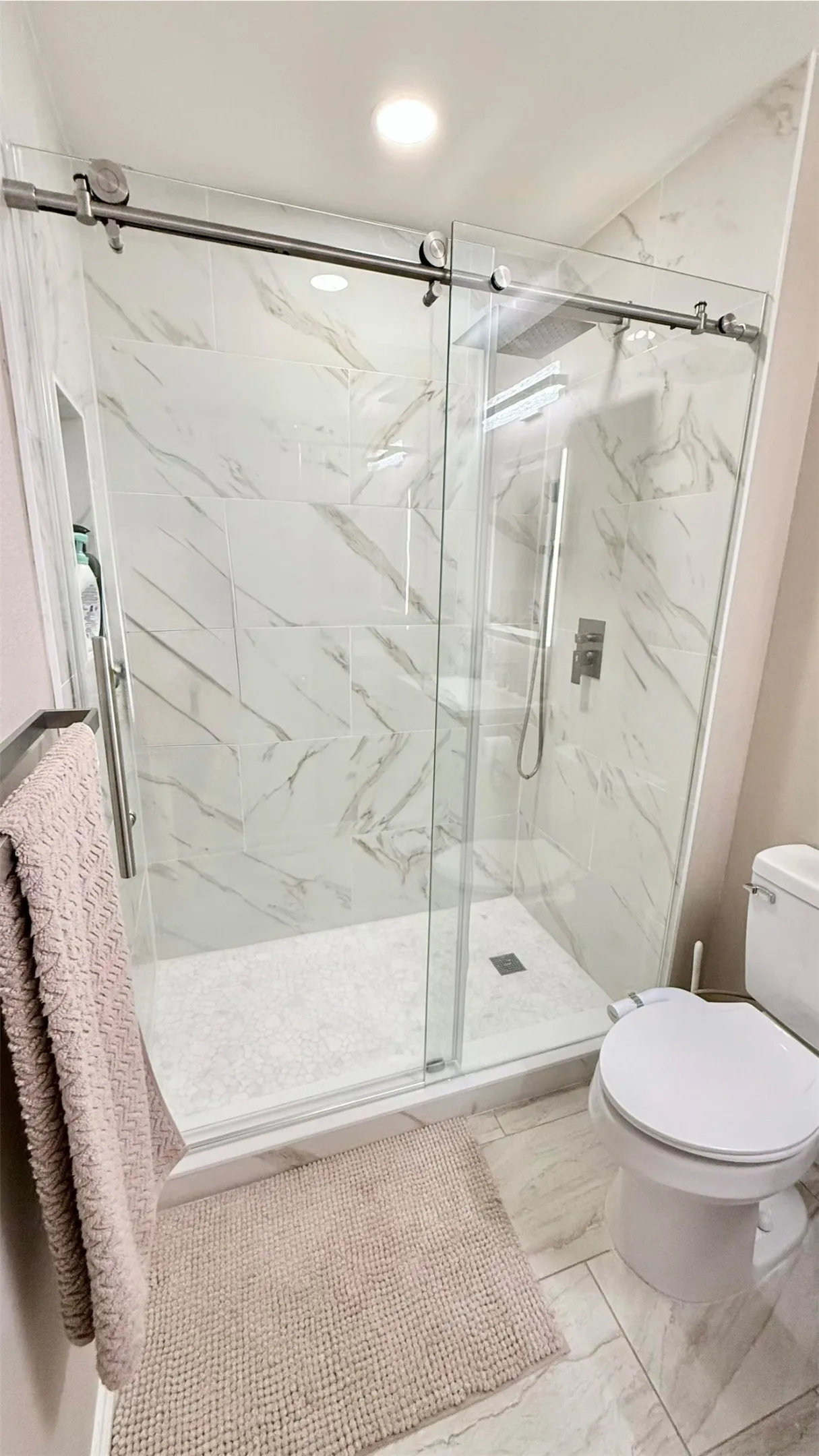 Shower enclosure featuring sliding glass doors with brushed nickel hardware, large format marble-look wall tiles, and a white tiled shower pan