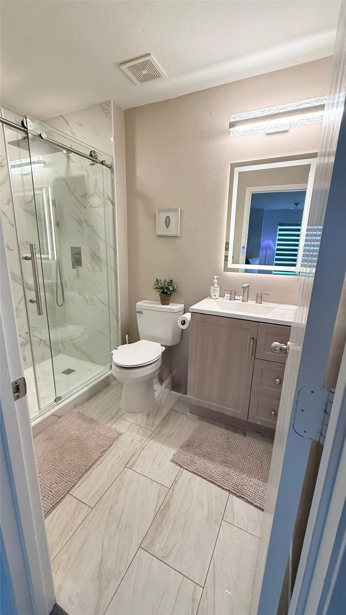 Bathroom featuring a glass-enclosed shower with tile surround, a single vanity with storage, tile flooring, and a lighted mirror