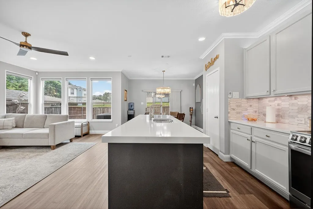 Kitchen island with a white countertop and integrated sink, light gray cabinetry with hardware, and an elongated hexagon tile backsplash