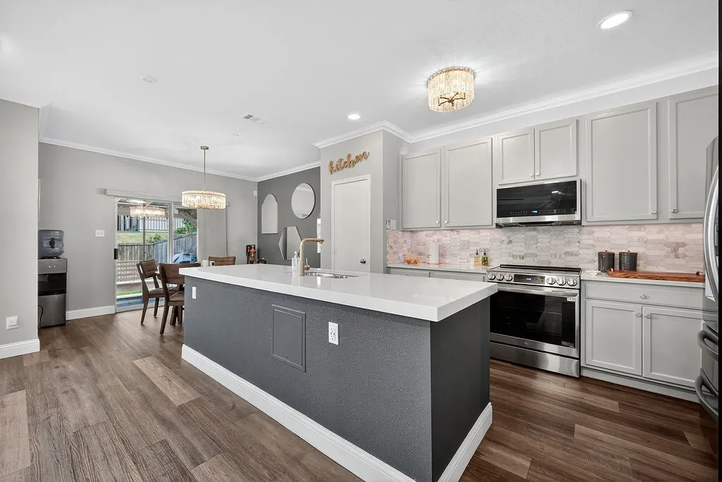 Central kitchen island with a white solid surface countertop, complemented by light gray cabinetry, stainless steel appliances, and wood-finish flooring