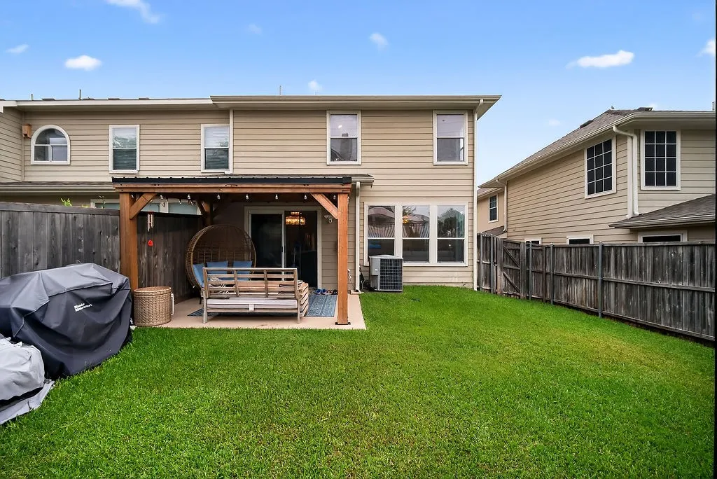 Expansive backyard featuring a lush lawn, concrete patio, and a built-in wooden pergola with string lighting