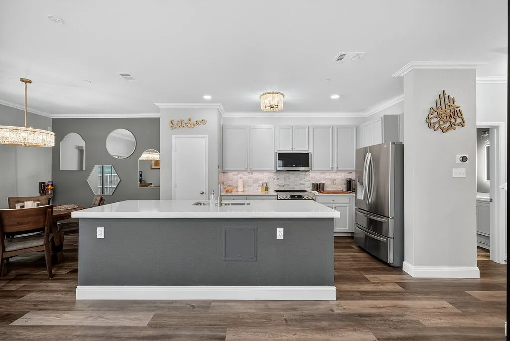 Spacious kitchen featuring a central island with white countertop, light gray cabinetry, stainless steel appliances, and wood-finish flooring