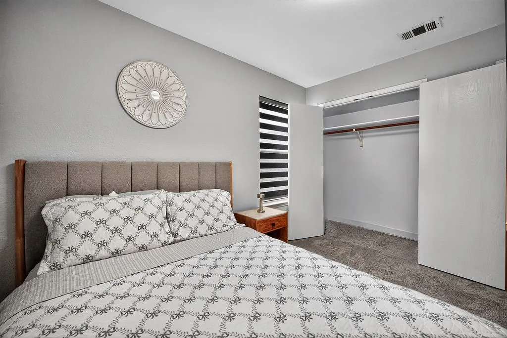 Bedroom featuring neutral-toned walls, textured carpet flooring, and a window with horizontal blinds