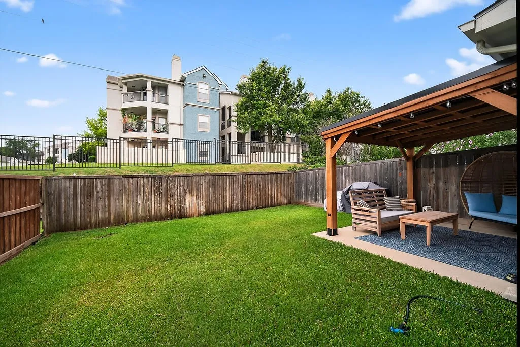 Outdoor patio featuring a wooden pergola with string lights, set on a concrete pad with a dark blue area rug