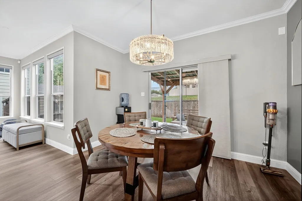Dining area featuring wood-finish flooring, a contemporary chandelier, multiple windows with white trim, and a sliding glass door