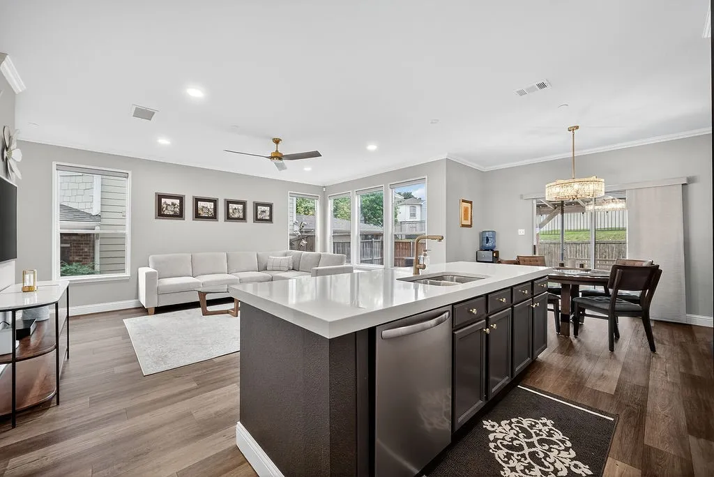 Spacious open-concept living area featuring a large kitchen island with a white countertop and dark cabinetry, wood-finish flooring, recessed lighting, and a ceiling fan