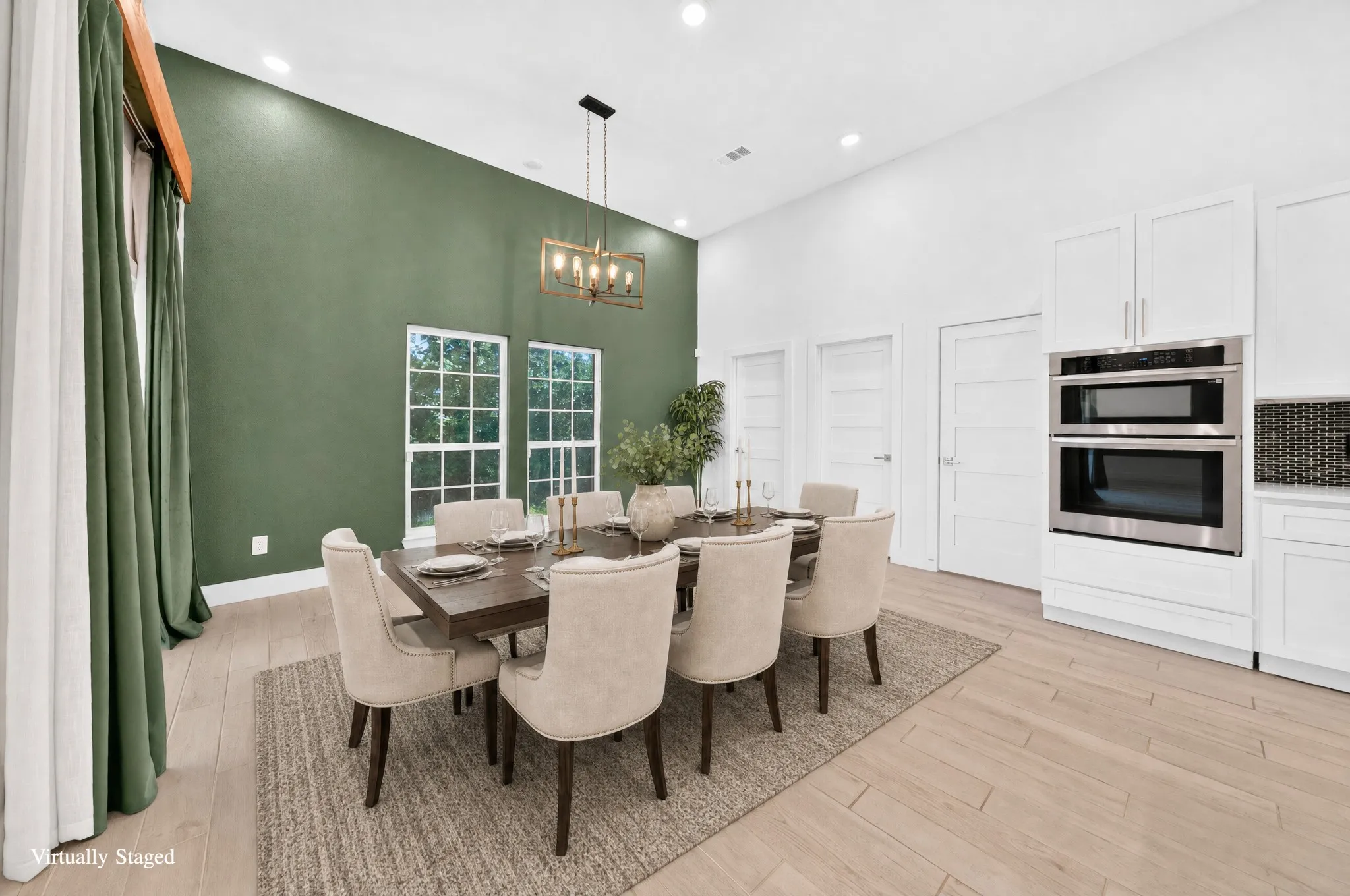 Dining area featuring high ceilings, wood-finish flooring, a contemporary chandelier, two large windows, and a built-in double oven appliance
