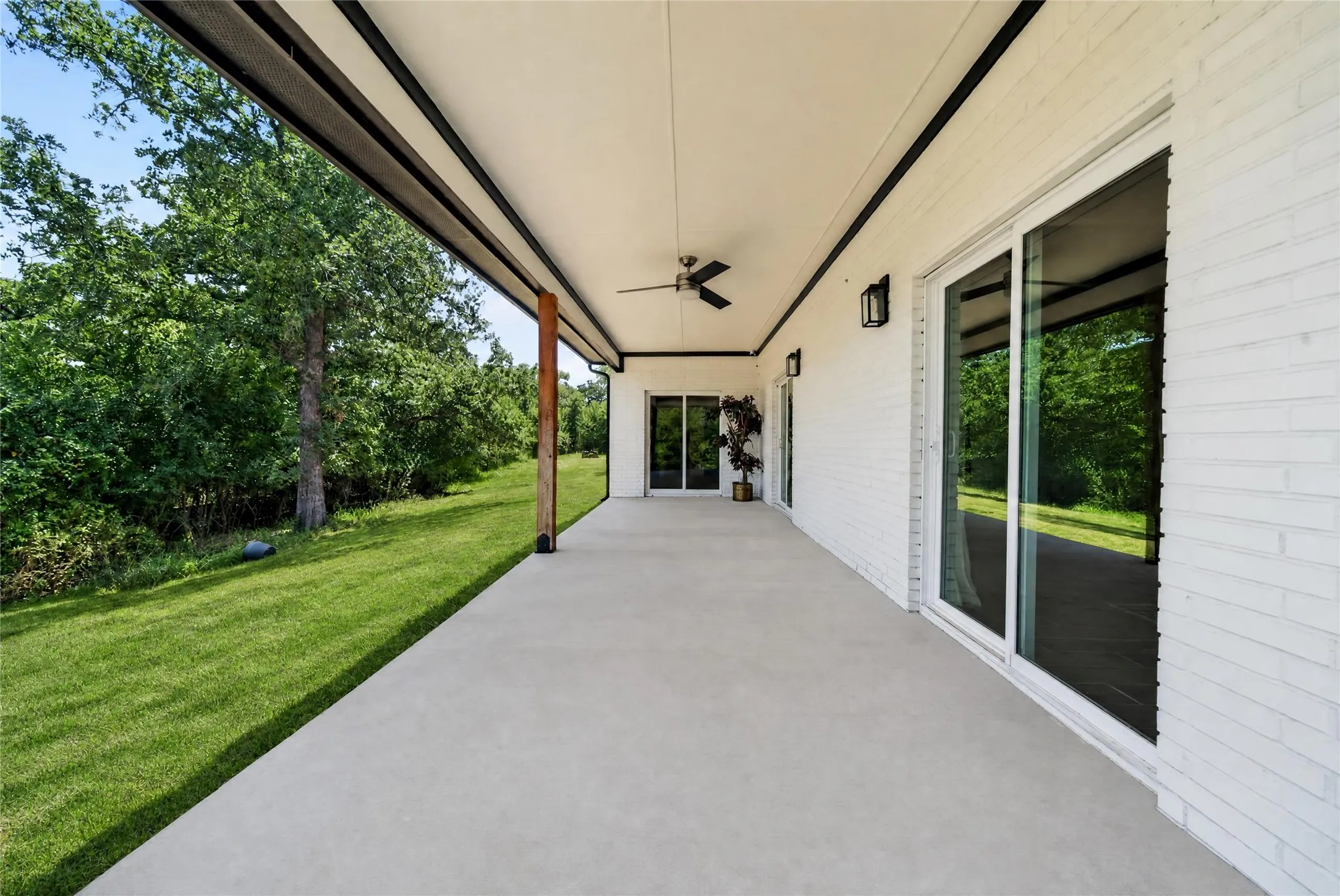 Expansive covered patio featuring a concrete surface, white brick exterior, black ceiling fan, and multiple sliding glass doors