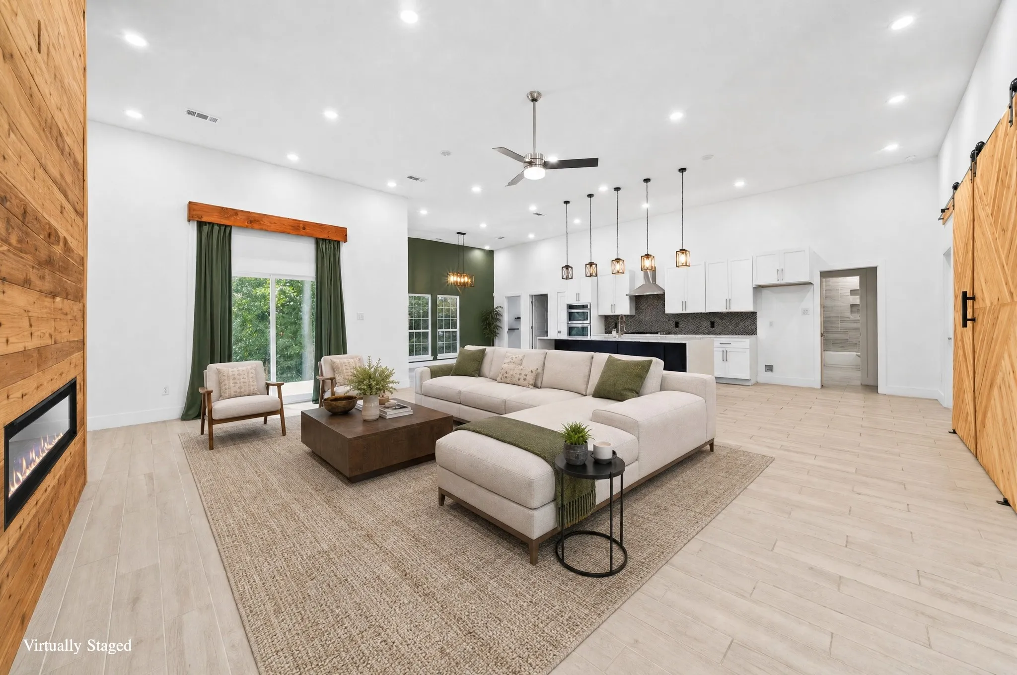Open-concept living area featuring light wood-finish flooring, a linear fireplace with wood paneling, recessed lighting, and a ceiling fan