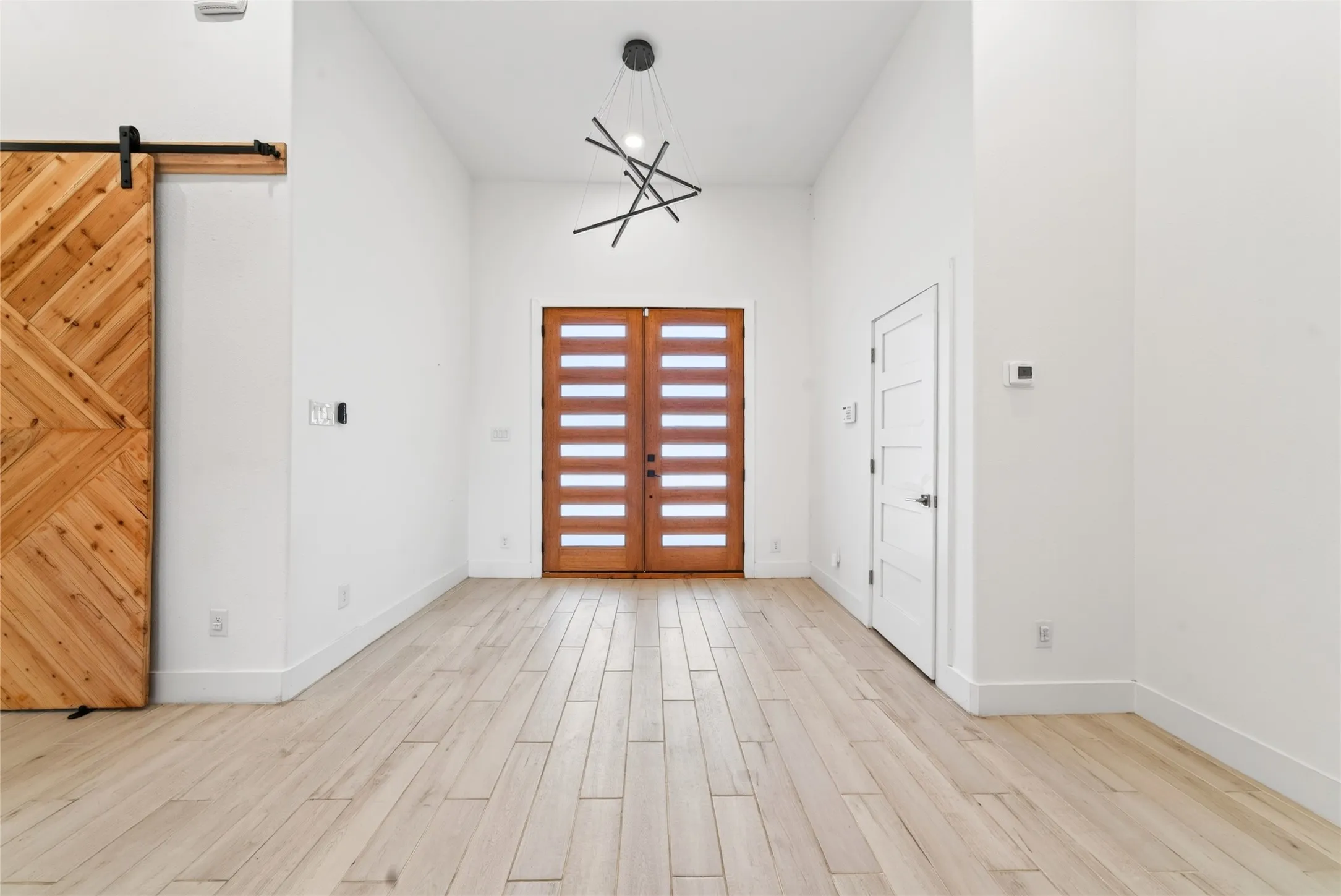Double entry doors with frosted glass panels, wood-finish flooring, and a contemporary linear chandelier